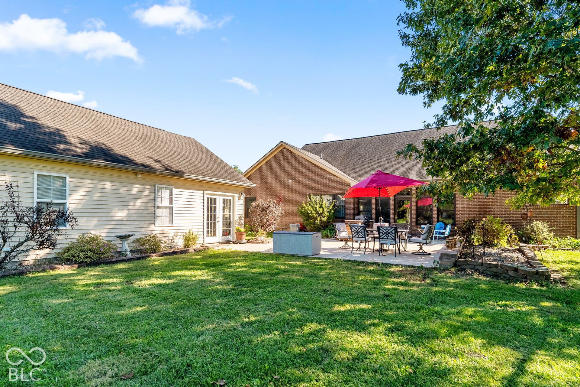 Expansive lawn with a stone-paved patio, mature trees, and a brick-faced exterior