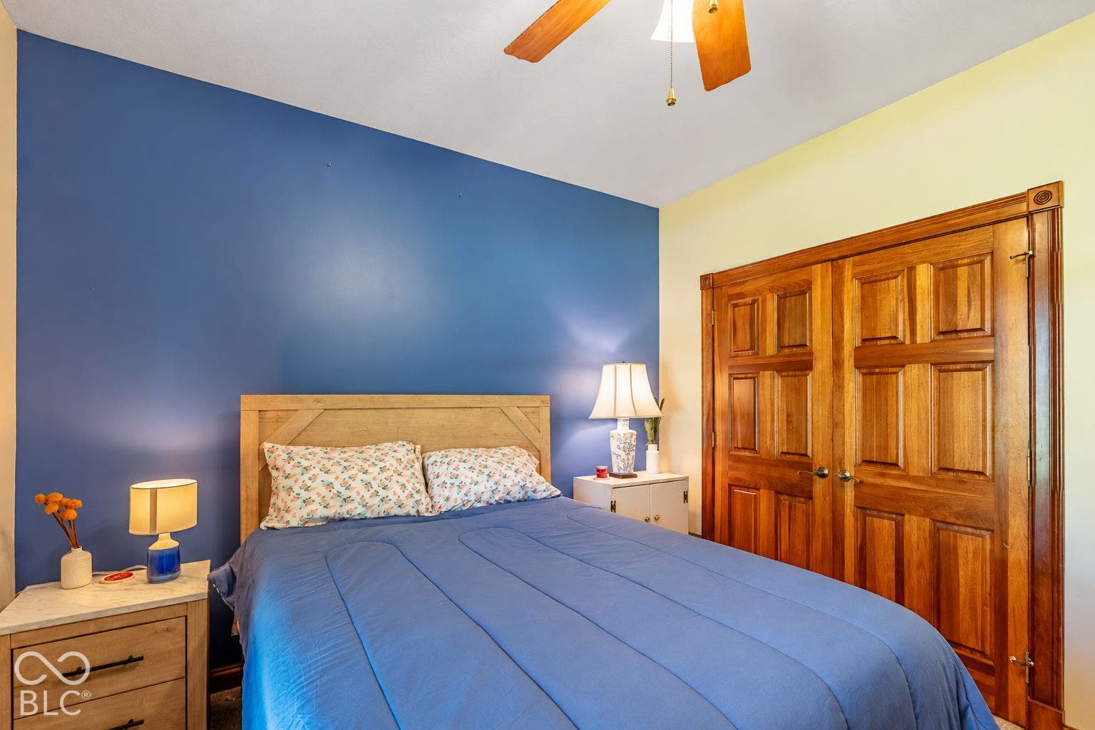 Wood panel closet doors, ceiling fan with integrated lighting, wood headboard, and a neutral ceiling