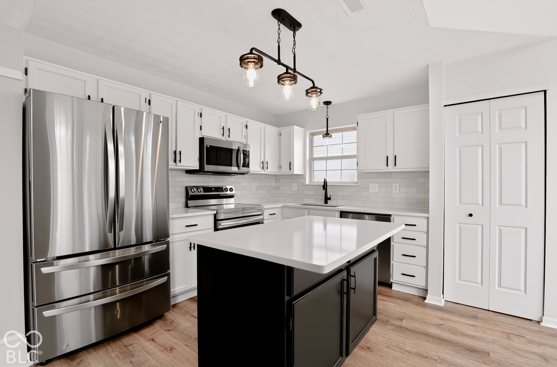 Kitchen featuring stainless steel appliances, white cabinetry with dark hardware, a center island with a white countertop, and wood-finish flooring