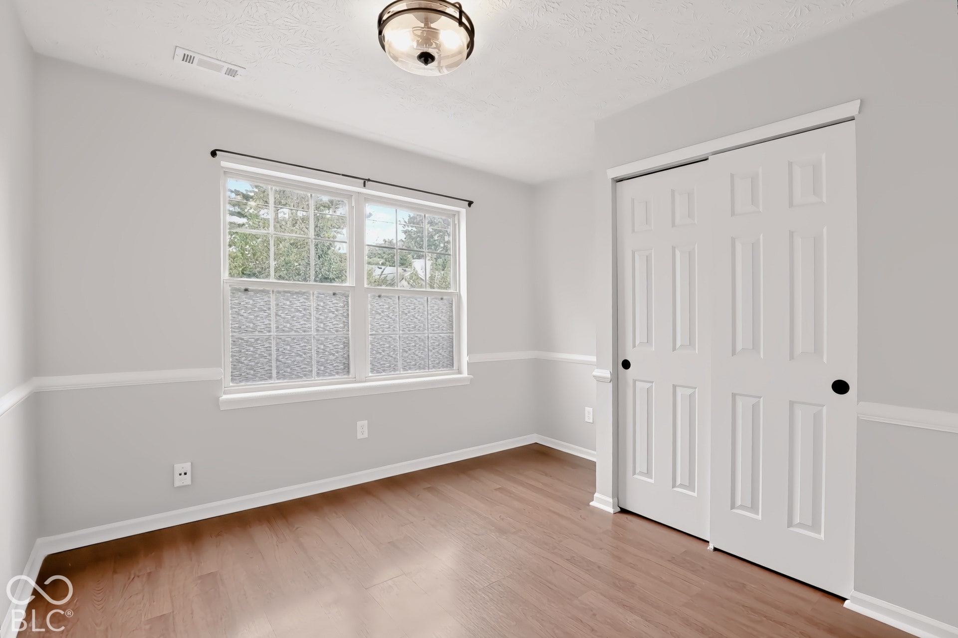 Wood-finish flooring, two-tone wall paint, white trim, a double-pane window, and a built-in closet with sliding panel doors