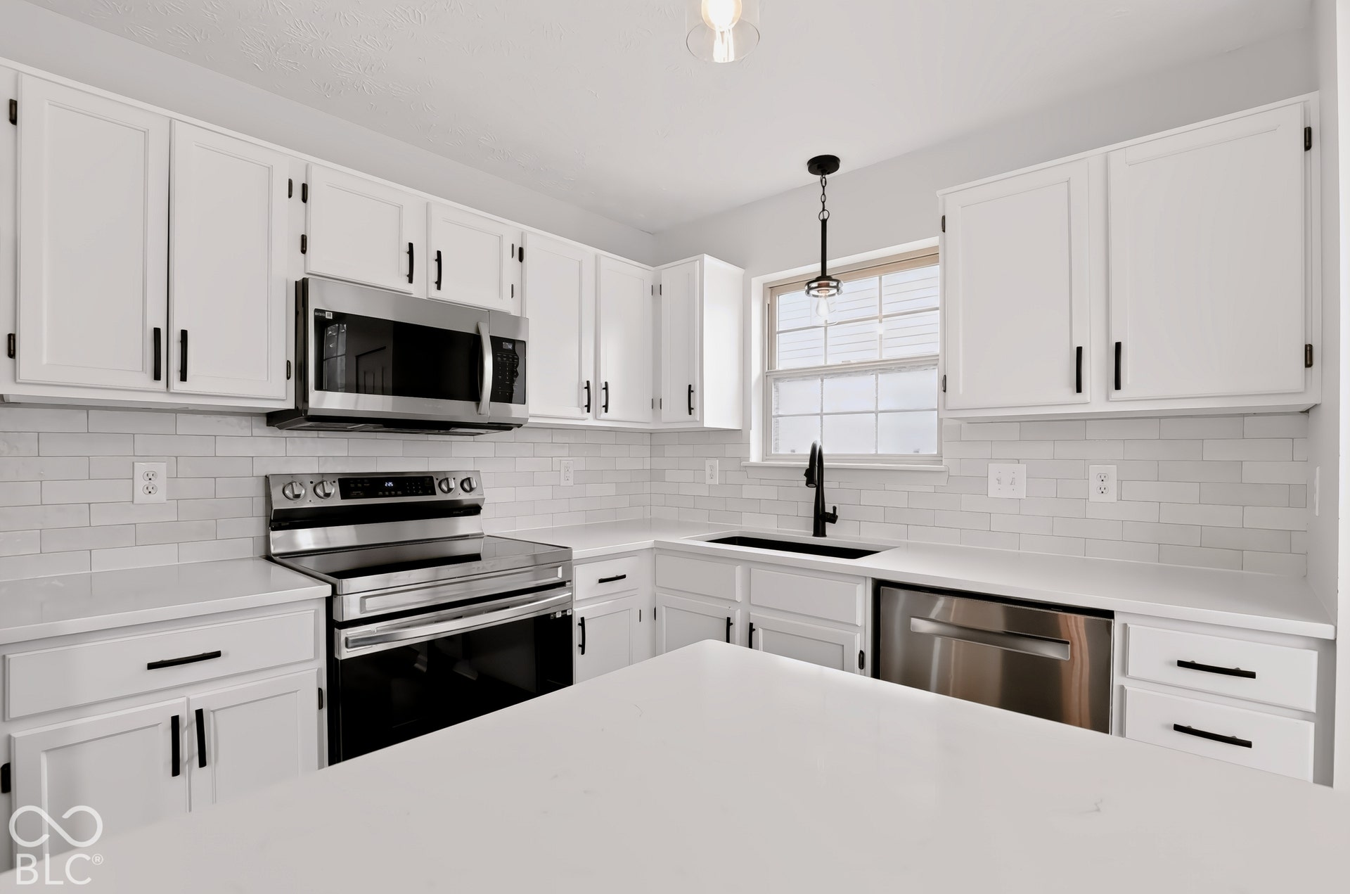 White shaker-style cabinetry with black hardware, stainless steel appliances, white subway tile backsplash, white countertops, and a black gooseneck faucet