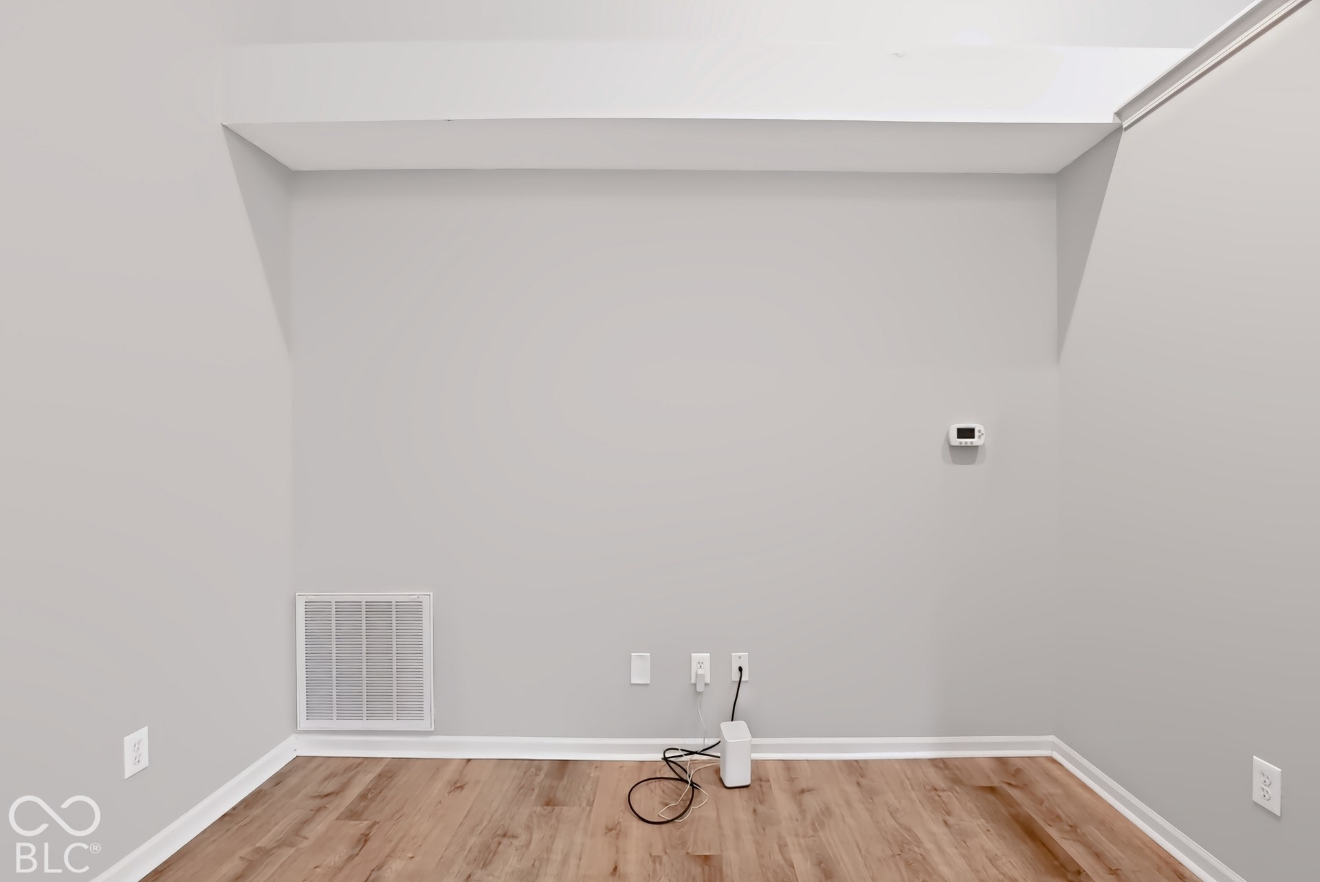 Bright, open room featuring wood-finish flooring, recessed ceiling with soffit detail, and multiple electrical outlets