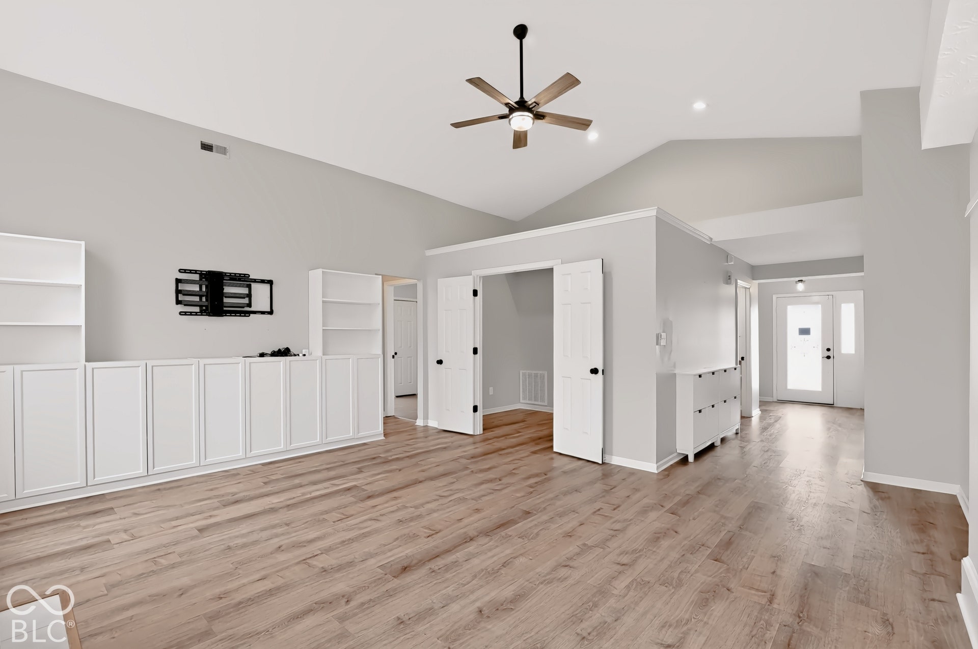 Vaulted ceilings complemented by a ceiling fan with light, wood-finish flooring, built-in cabinetry, and white paneled doors