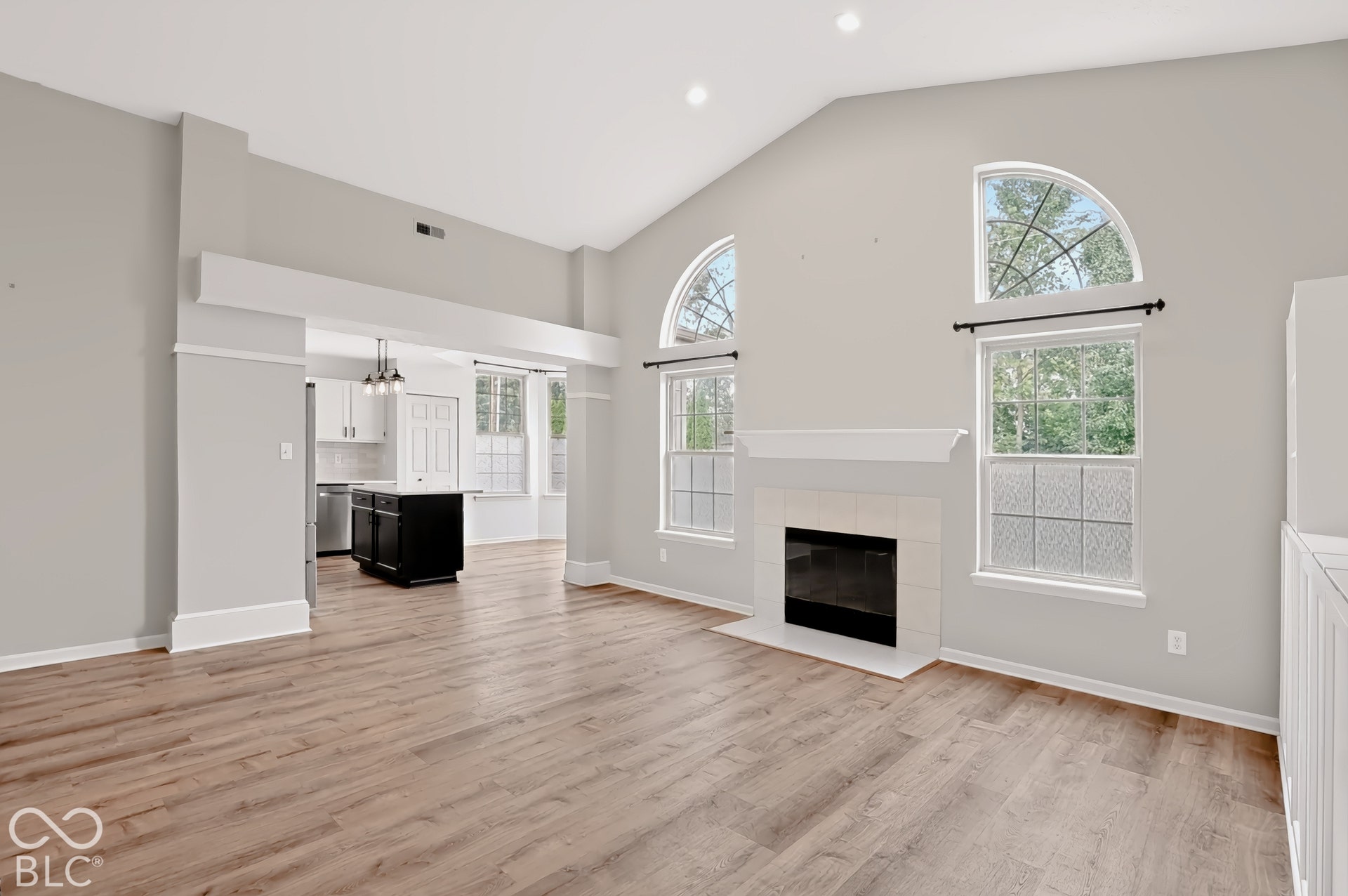 Vaulted ceiling, wood-finish flooring, fireplace with tile surround, arched transom windows, and recessed lighting