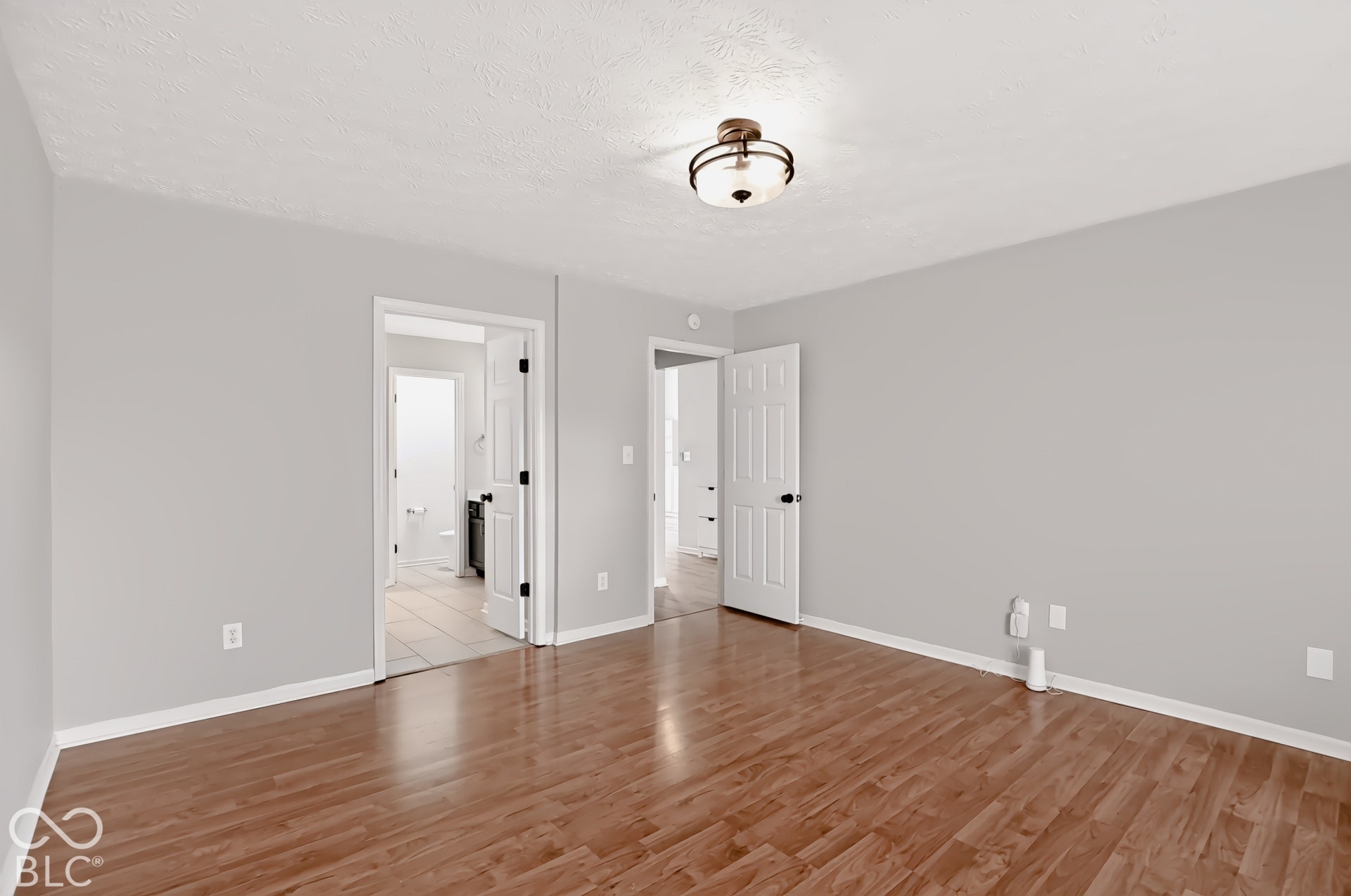 Bright, open room showcasing gleaming wood-finish flooring, white six-panel doors with black hardware, soft recessed lighting, and neutral painted walls