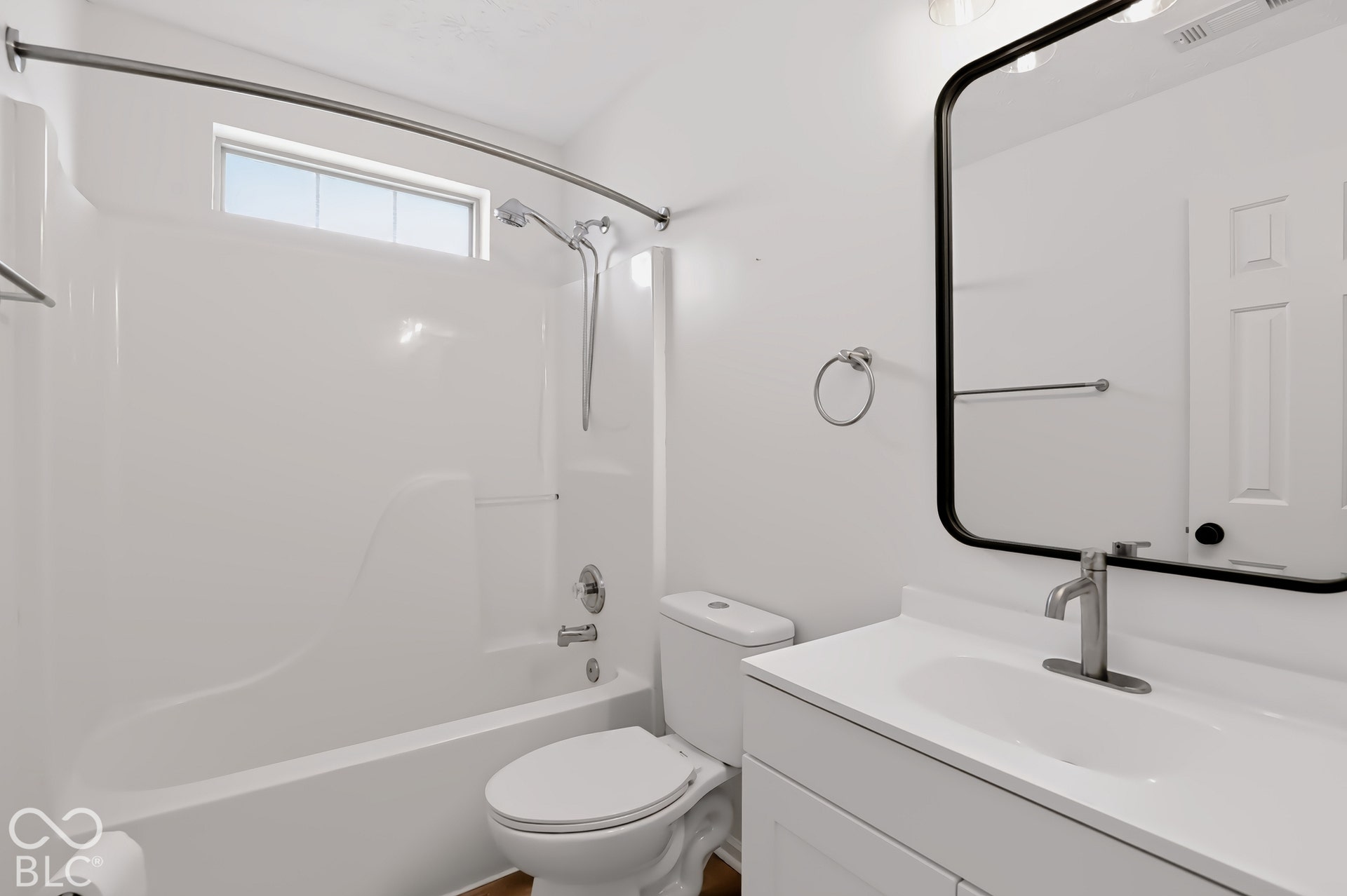 White vanity with an integrated sink and brushed nickel faucet, a black-framed rectangular mirror, and a white tub/shower combination with a curved shower rod