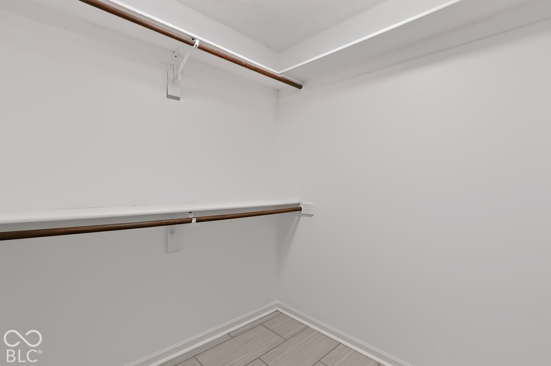 White walls, two levels of shelving, two clothing rods, and tile flooring