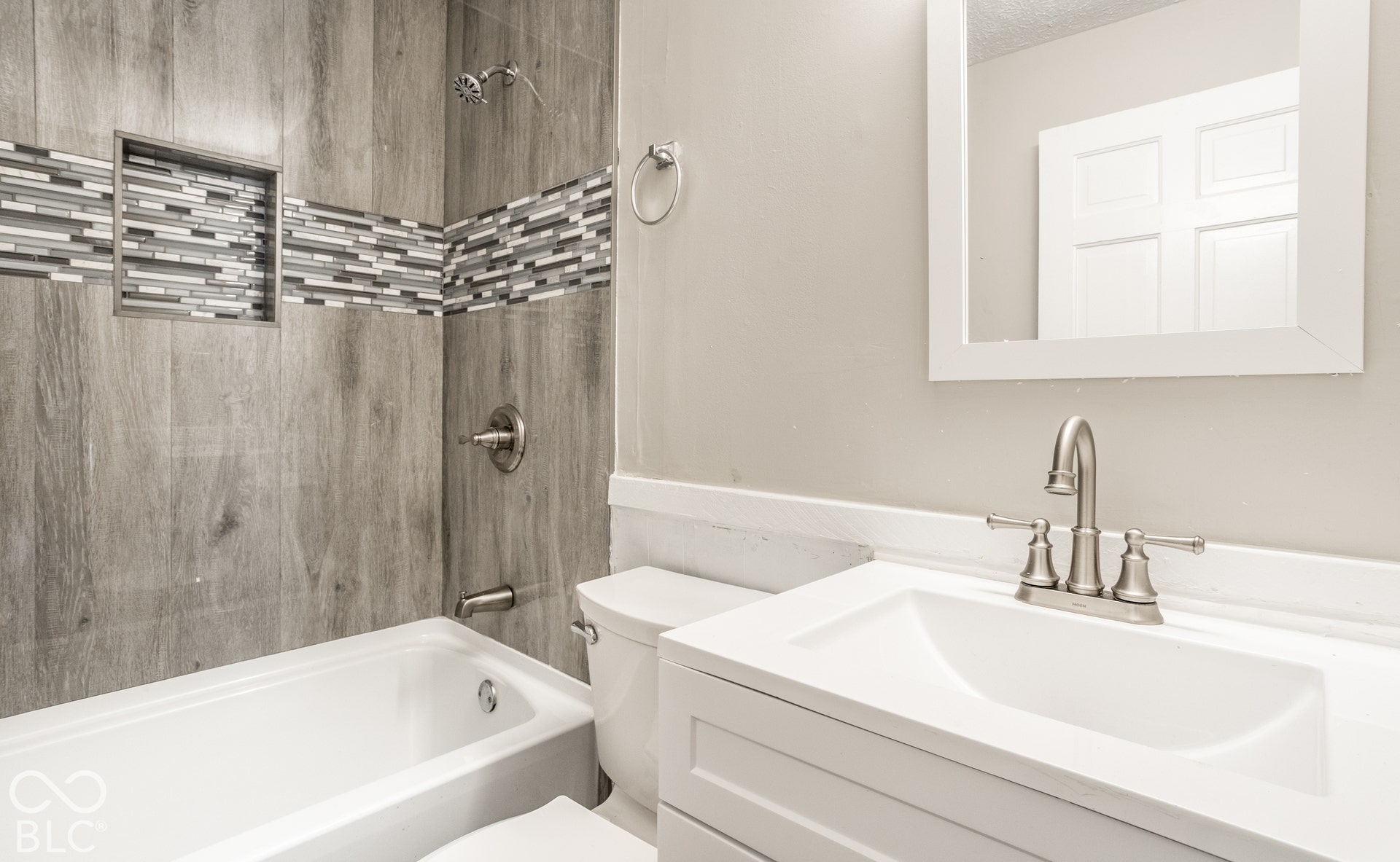 Bathroom featuring a white vanity with integrated sink, brushed nickel faucet, and framed mirror