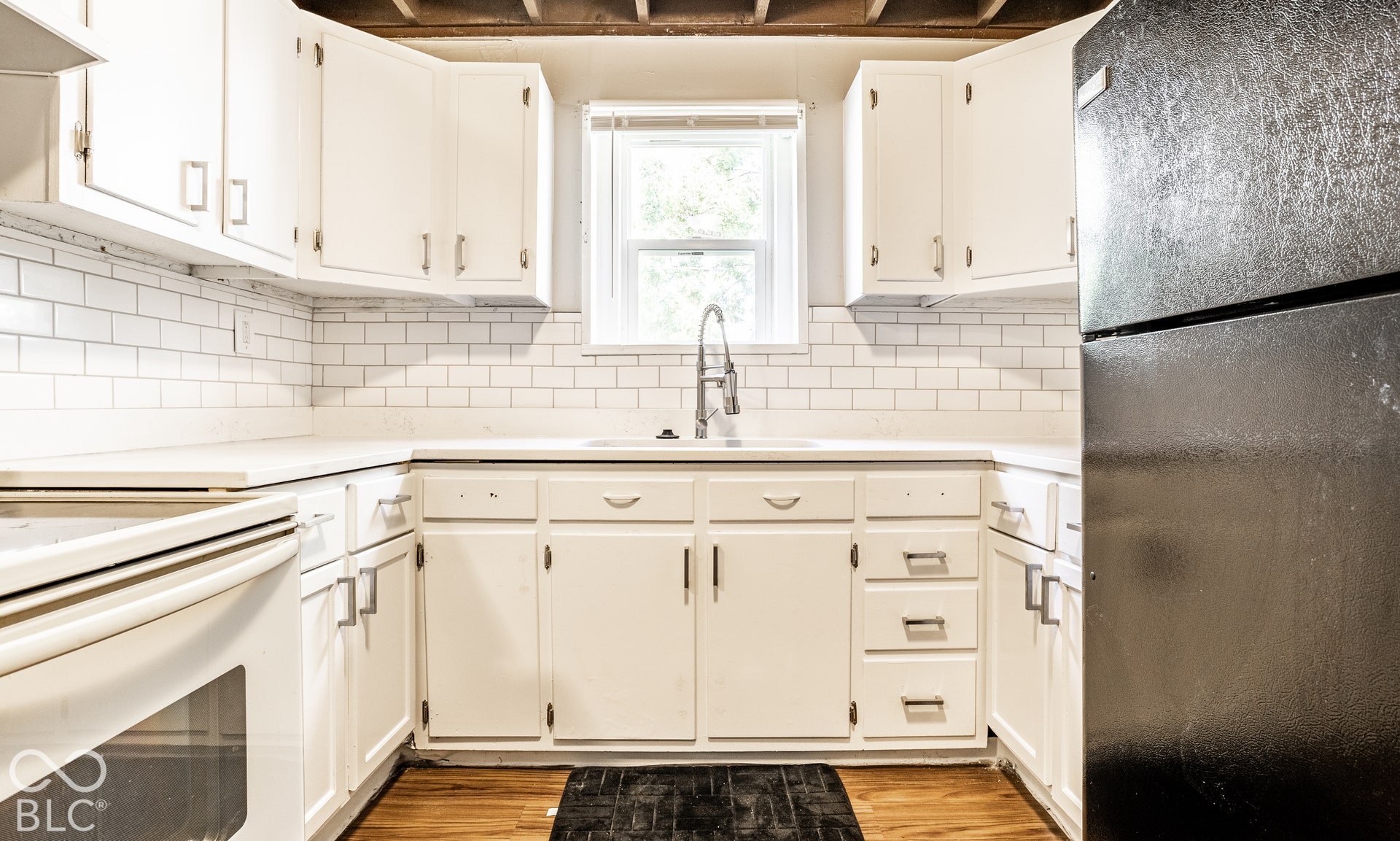 White cabinetry, white subway tile backsplash, white countertops, built-in sink, and wood-finish flooring