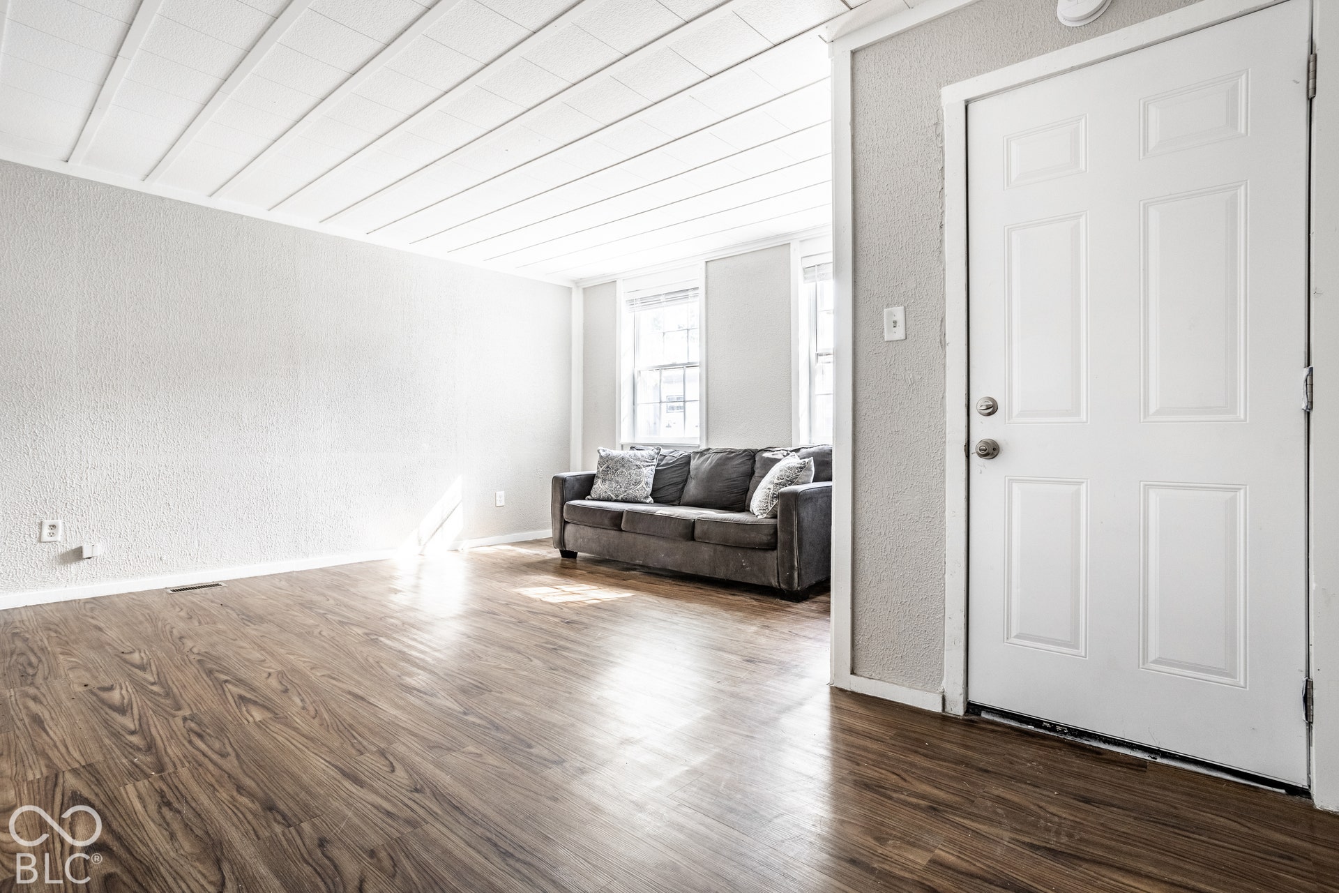 Wood-finish flooring, white panel ceiling, white interior door with paneling, and multiple windows