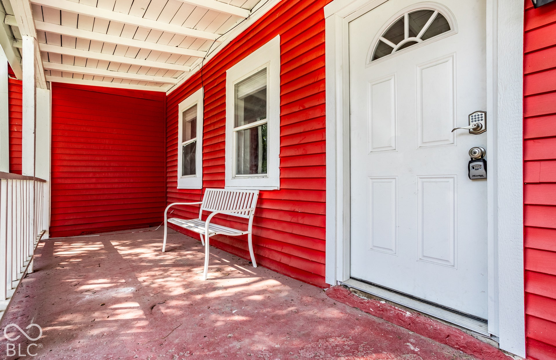 Front porch with red siding, white trim windows, white porch railing, and a white paneled entry door with an arched transom