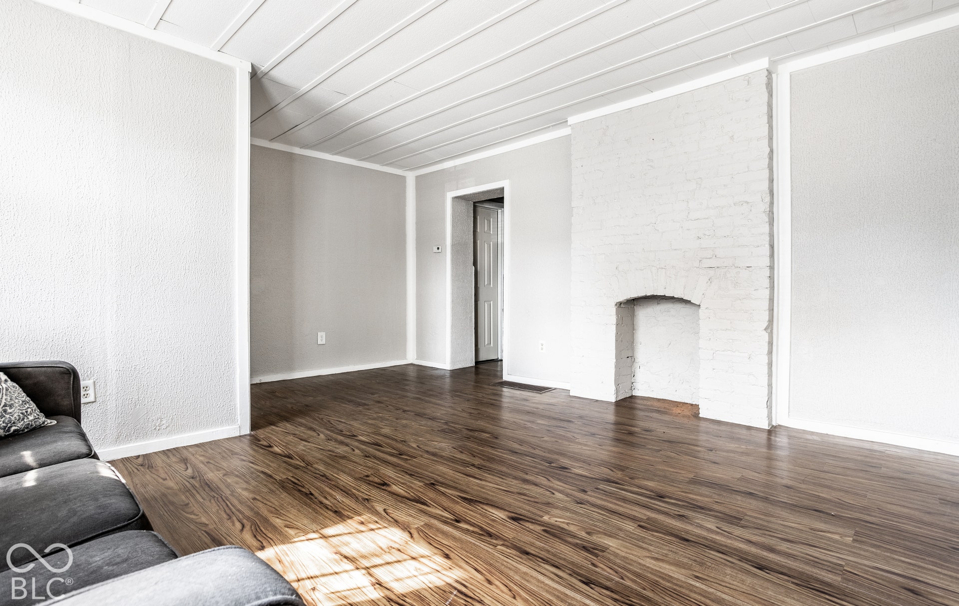 Wood-finish flooring, white painted brick fireplace, textured walls, and a beamed ceiling