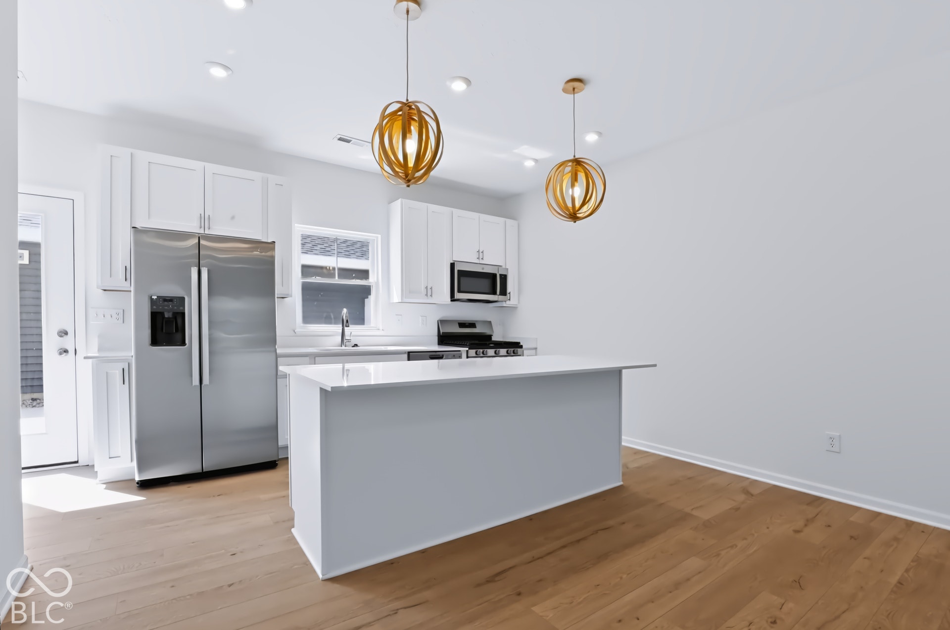 Gourmet kitchen featuring stainless steel appliances, white cabinetry, a center island, wood-finish flooring, and contemporary pendant lighting