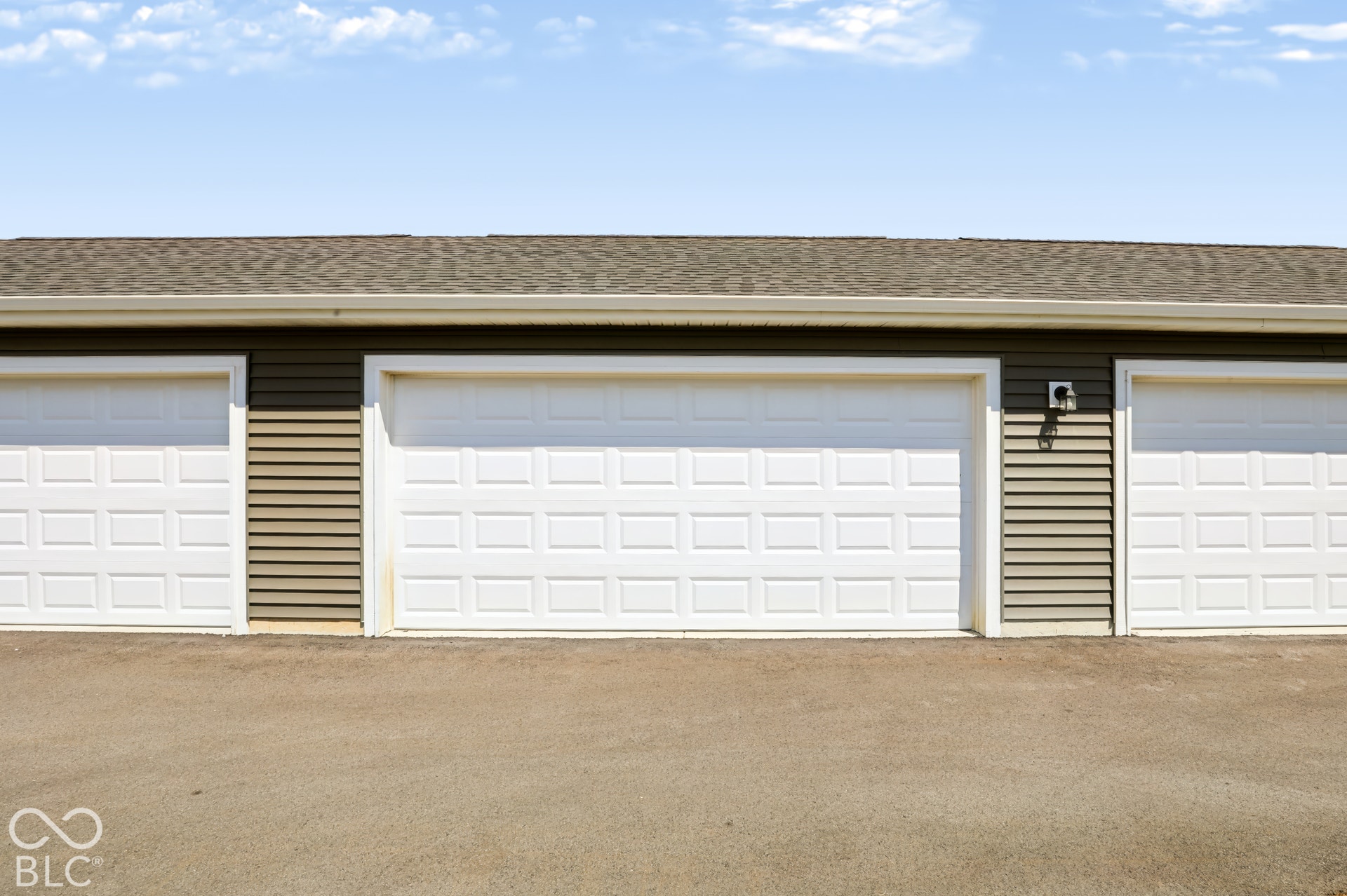 Three white panel garage doors with tan horizontal siding