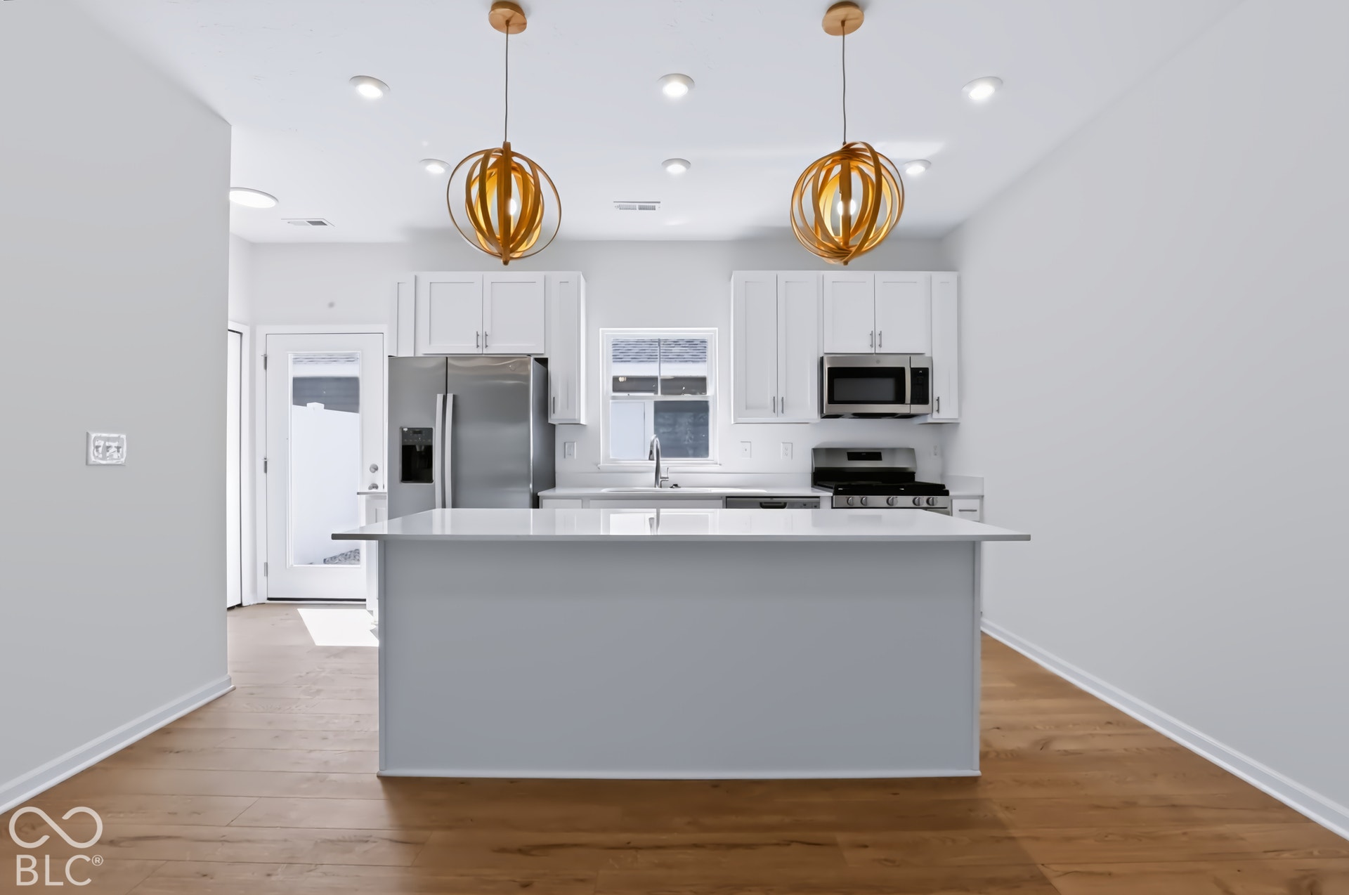 Kitchen featuring wood-finish flooring, white cabinetry, stainless steel appliances, and a central island with a light-colored countertop