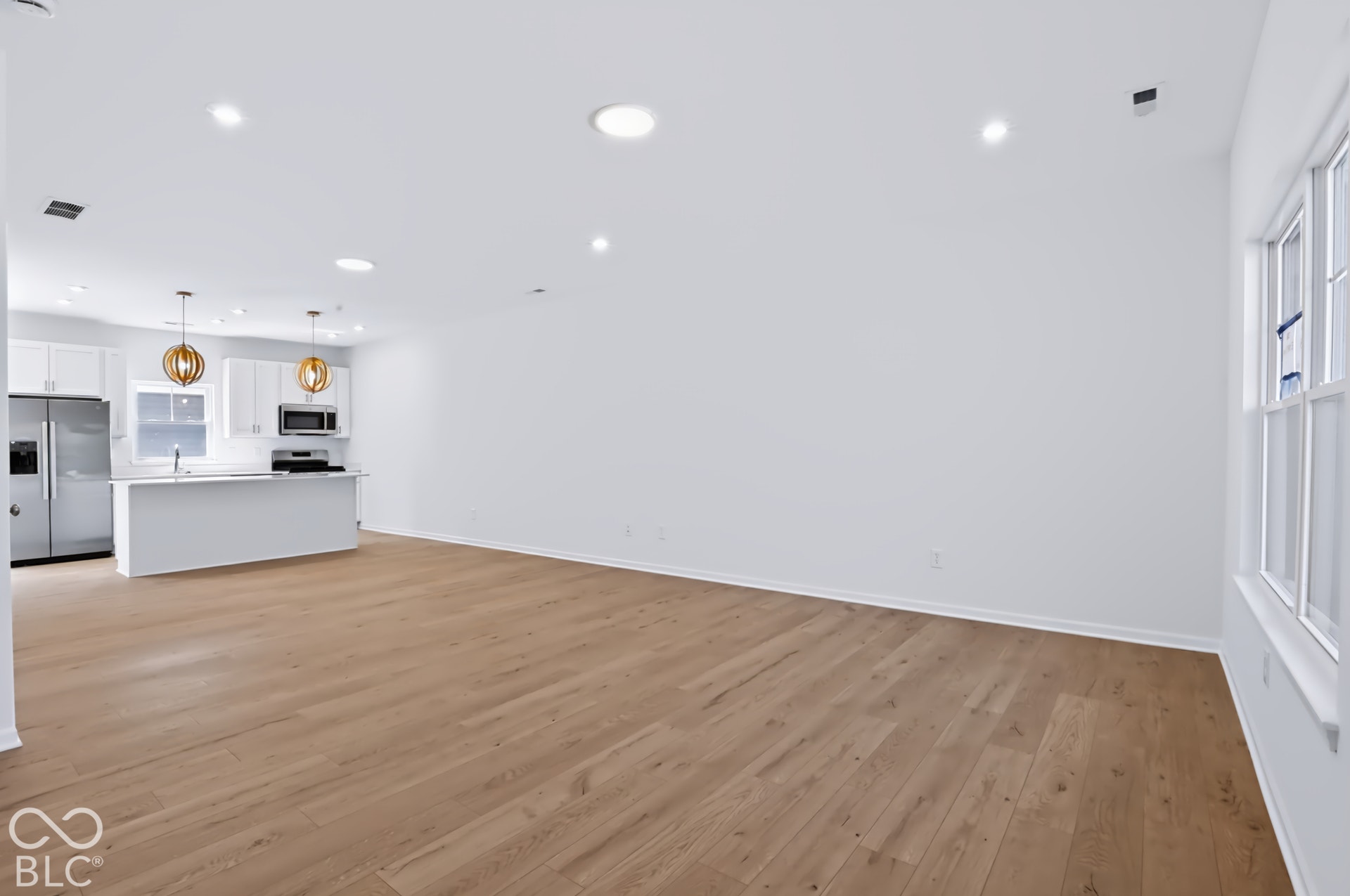 Open-concept living space with wood-finish flooring, recessed lighting, and a kitchen featuring white cabinetry and stainless steel appliances