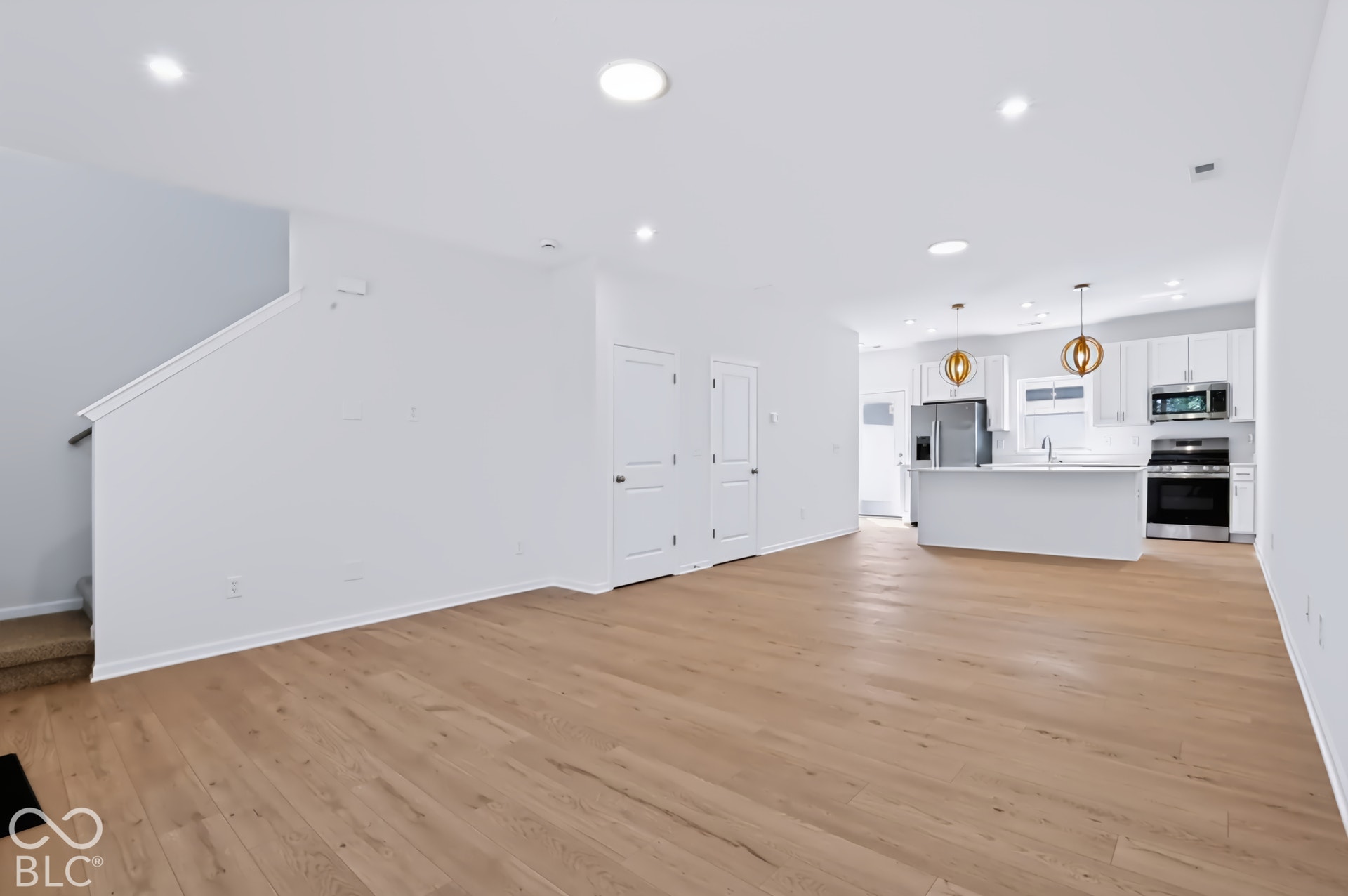 Recessed lighting, wood-finish flooring, white cabinetry, stainless steel appliances, and a kitchen island with pendant lighting
