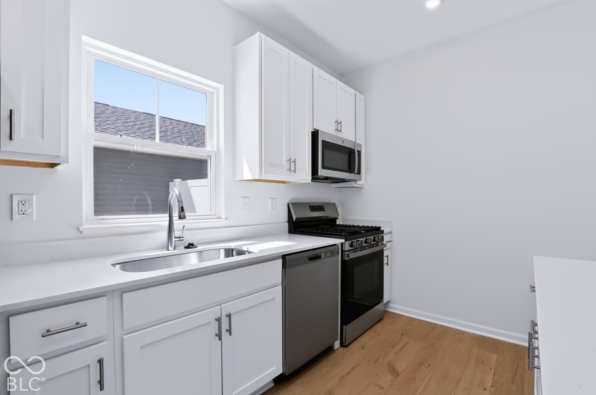 White shaker-style cabinetry with chrome hardware, stainless steel appliances, a gas range, a stainless steel sink with a high-arc faucet, and light wood-finish flooring
