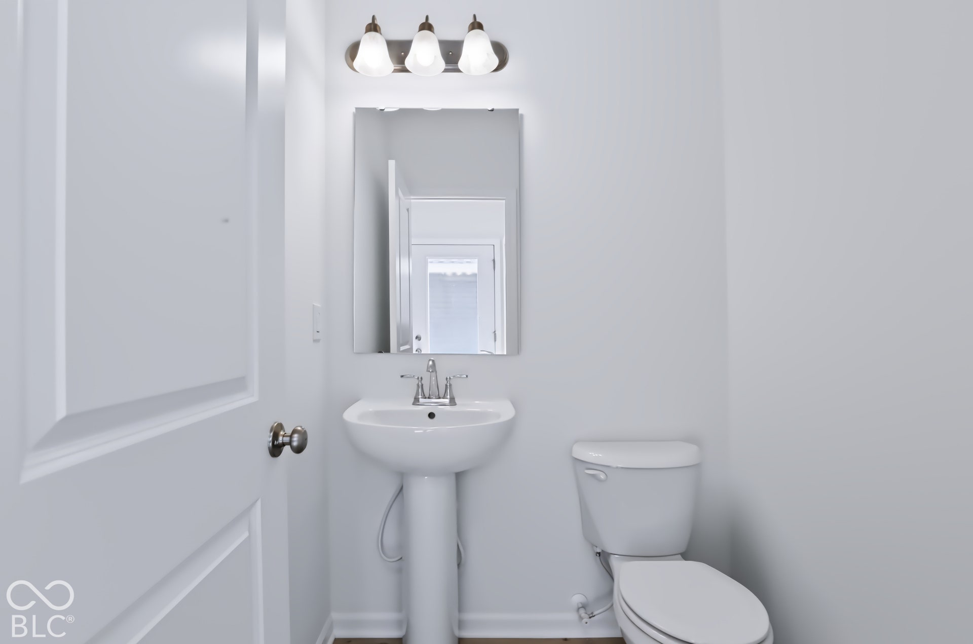 Pedestal sink with chrome fixtures, wall-mounted mirror, and overhead vanity lighting