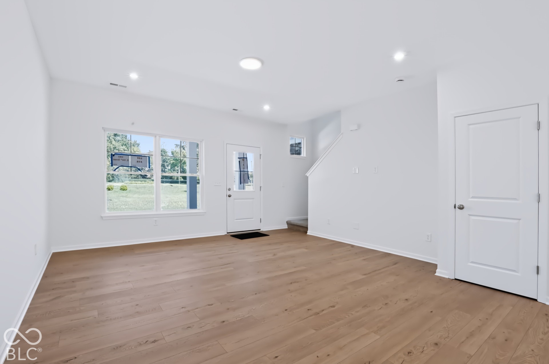 Recessed ceiling lighting, wood-finish flooring, white painted walls, white trim, and a white rear door with a frosted glass panel