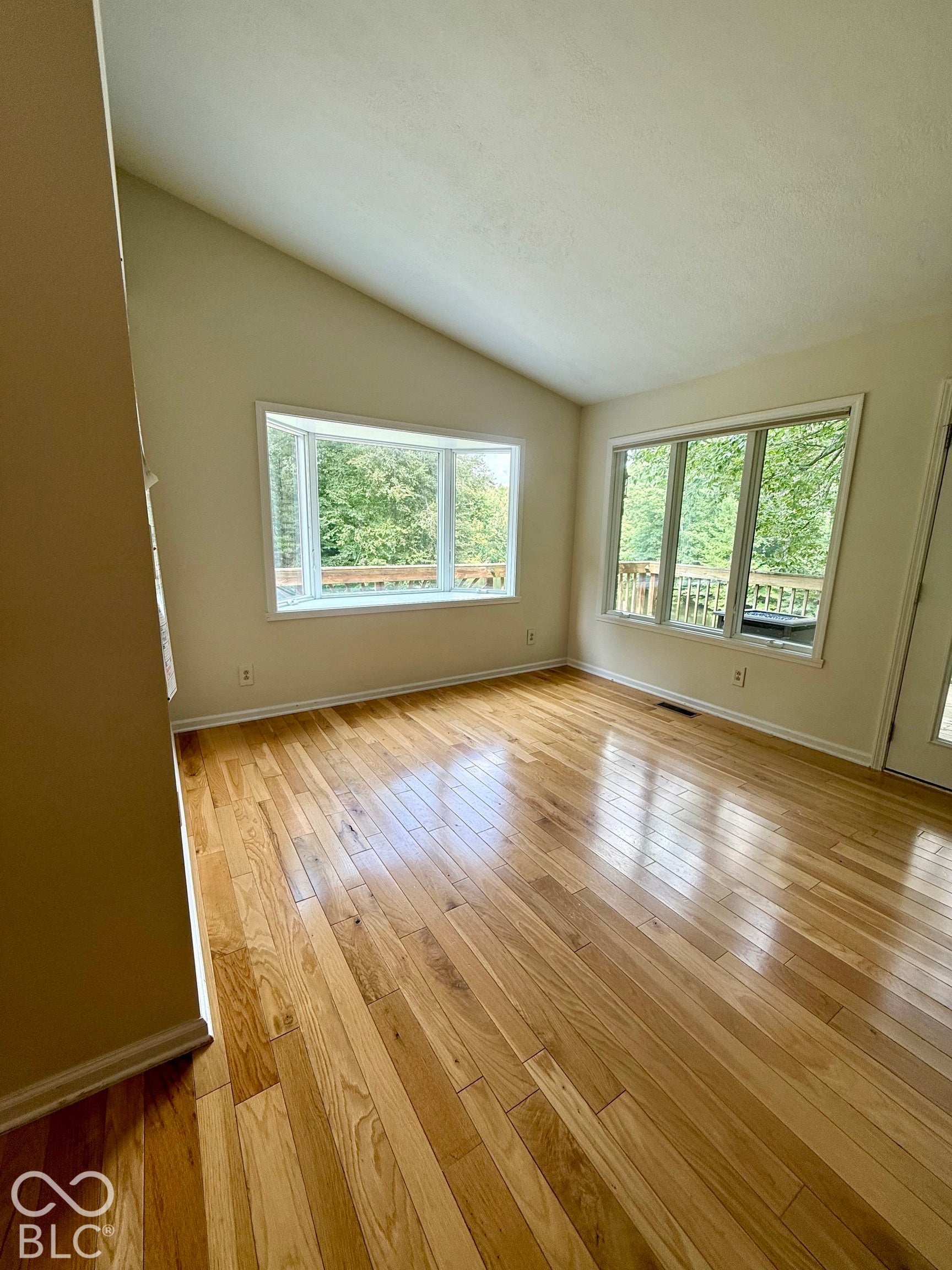 Vaulted ceiling, wood-finish flooring, and large bay windows.