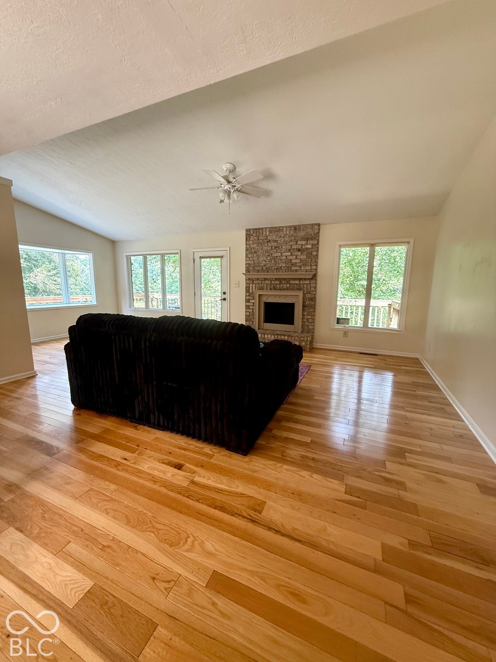 Vaulted ceiling, wood-finish flooring, brick-surround fireplace, ceiling fan, and multiple windows