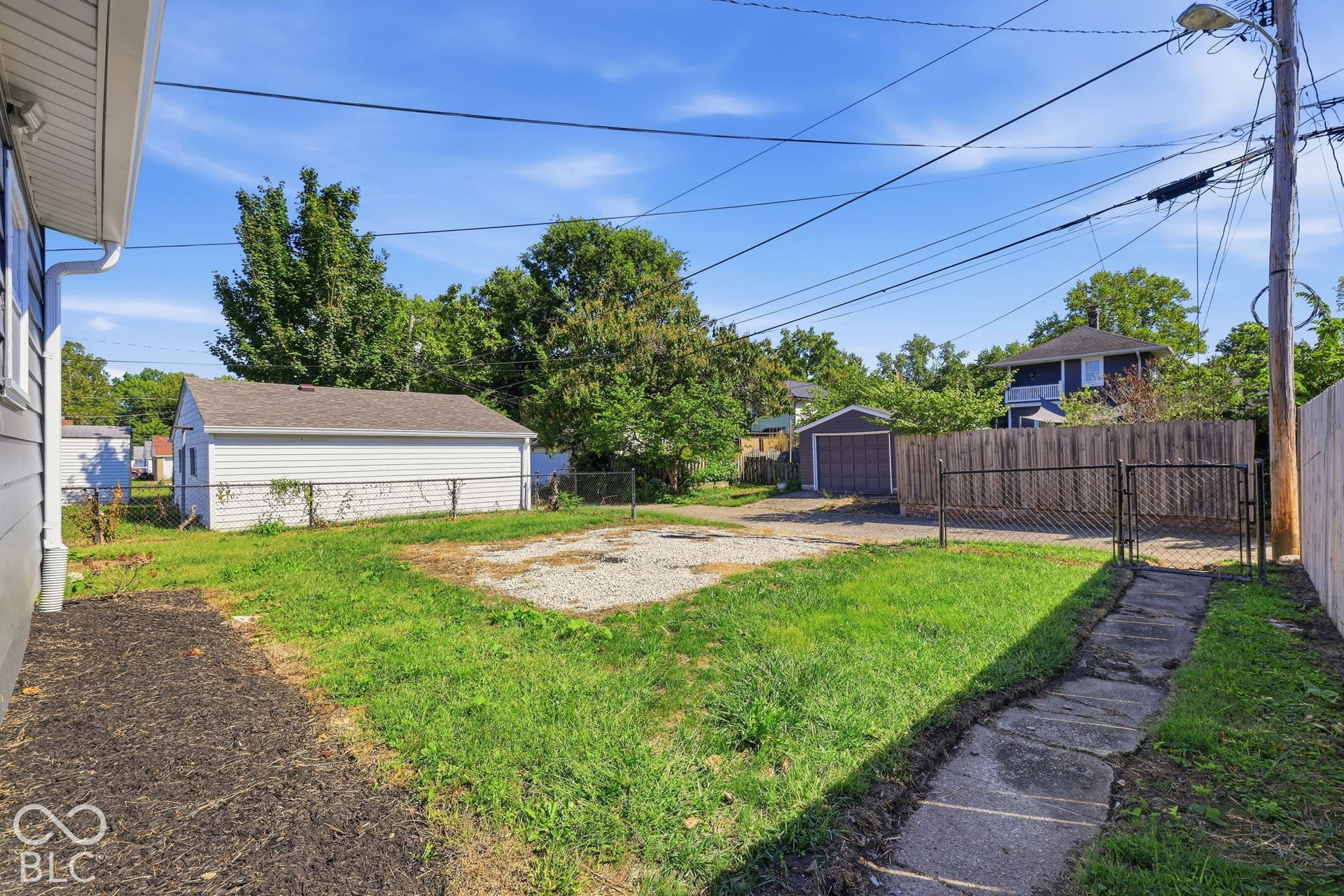 Rear yard with a detached garage, gravel parking area, and a wood privacy fence with a metal gate
