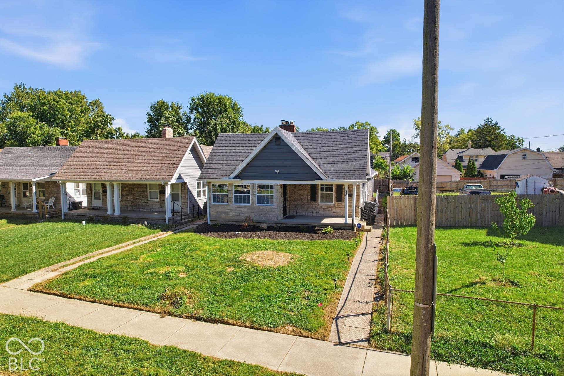 Exterior featuring gray siding, stone facade, a covered front porch, and a dark shingle roof
