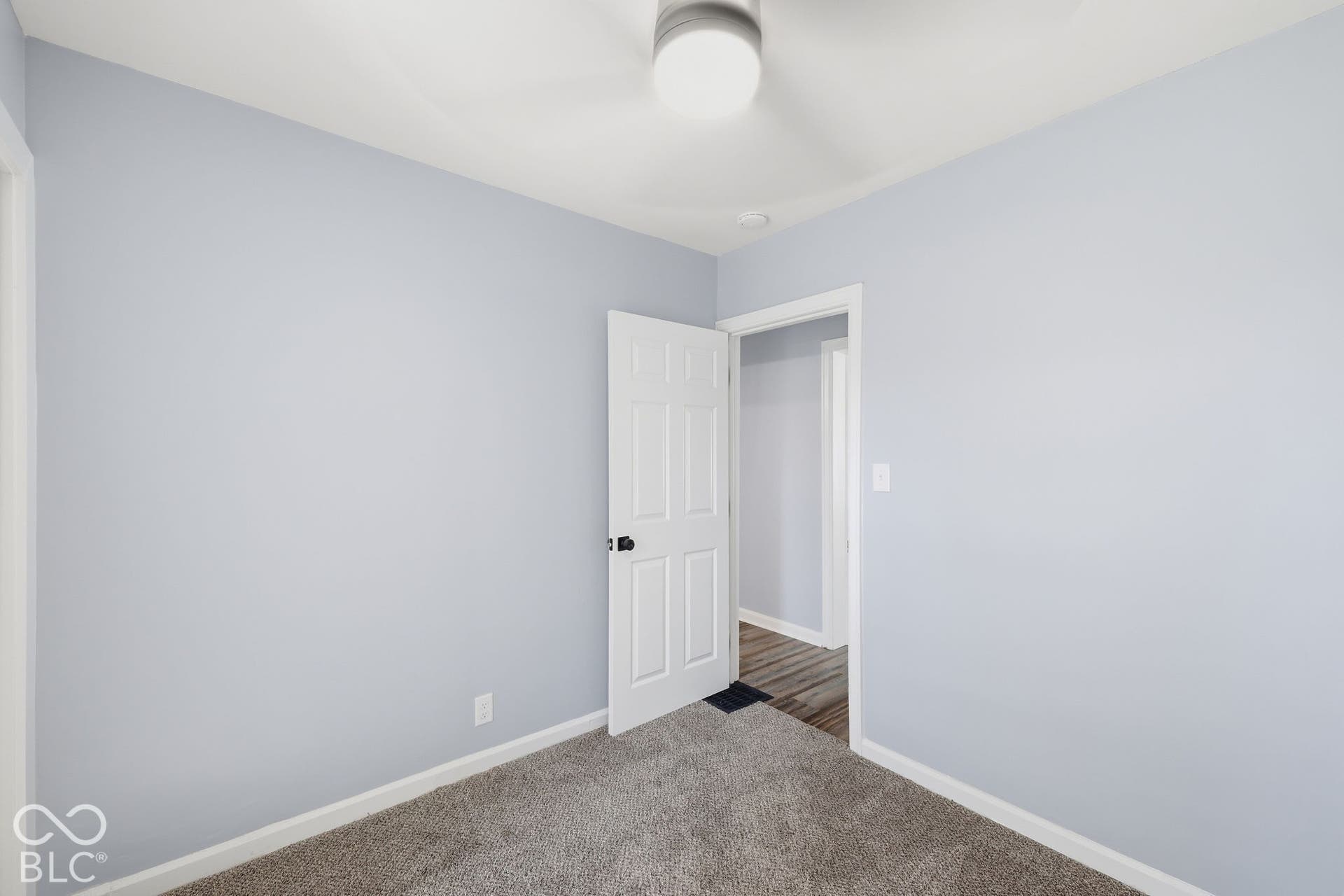 Plush carpet flooring, light blue wall paint, white trim, recessed ceiling light, and a white interior door with black hardware