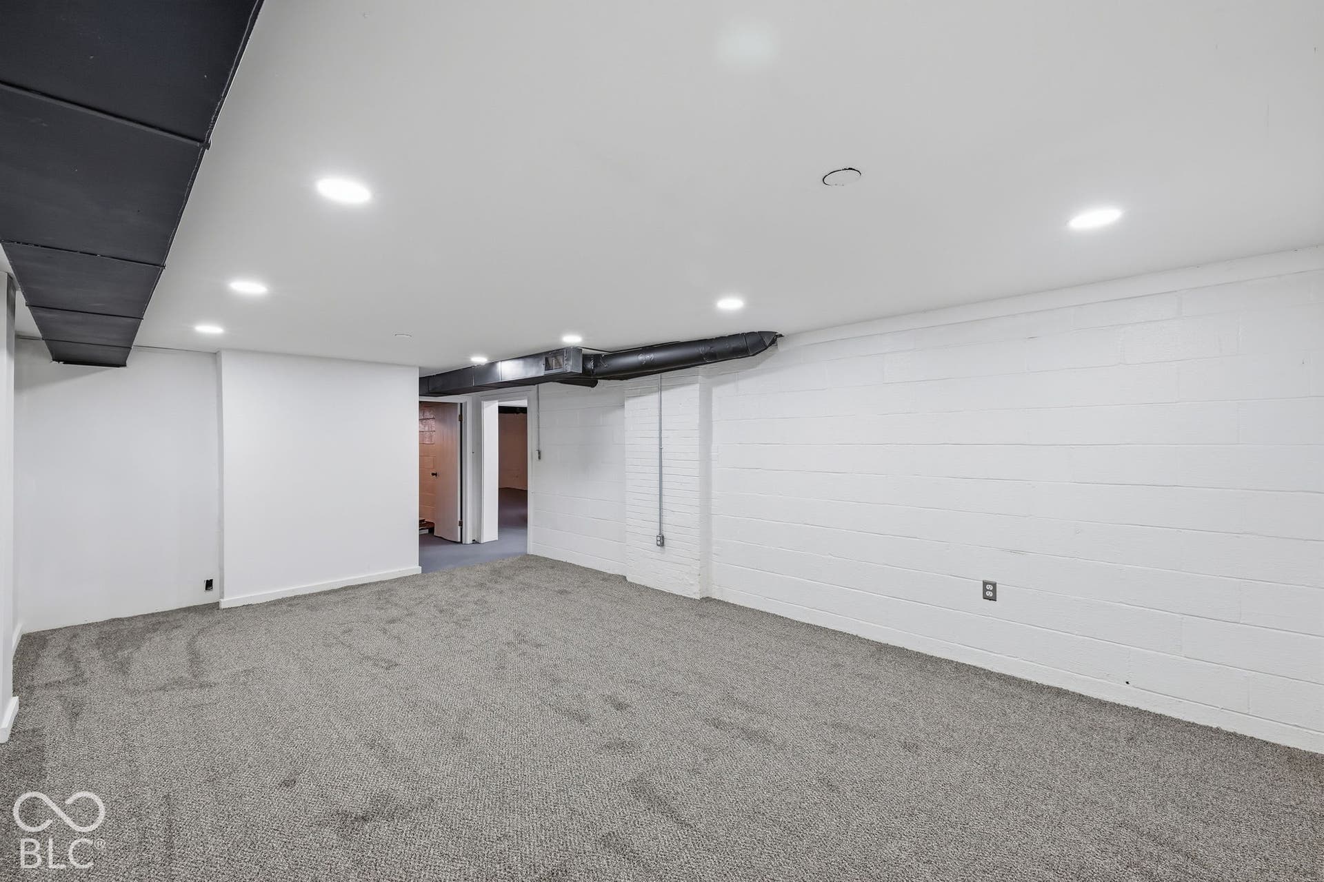 Recessed lighting illuminates the carpeted room, featuring white painted walls and exposed ductwork