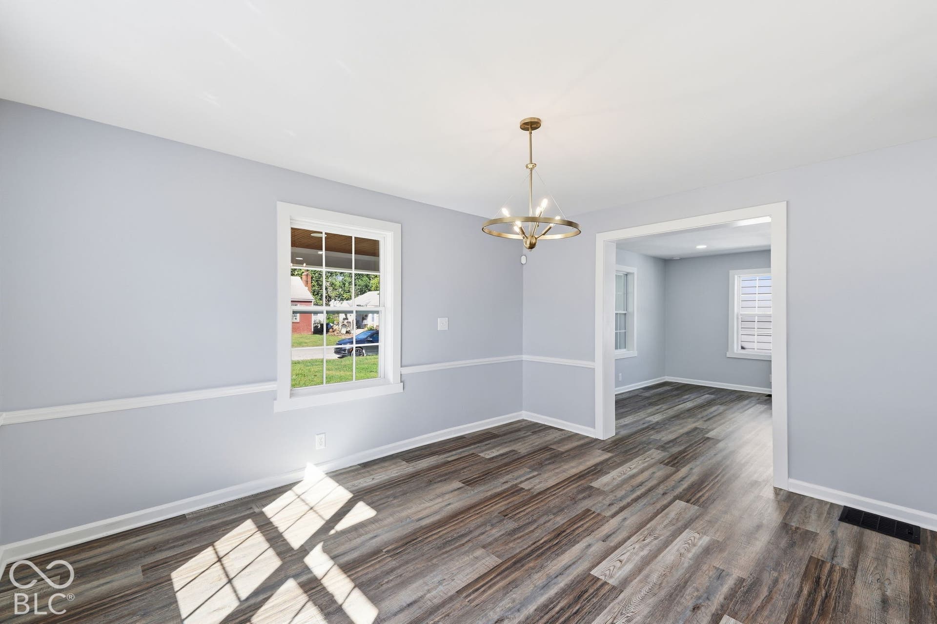 Wood-finish flooring, light gray wall paint, white trim, and a contemporary chandelier
