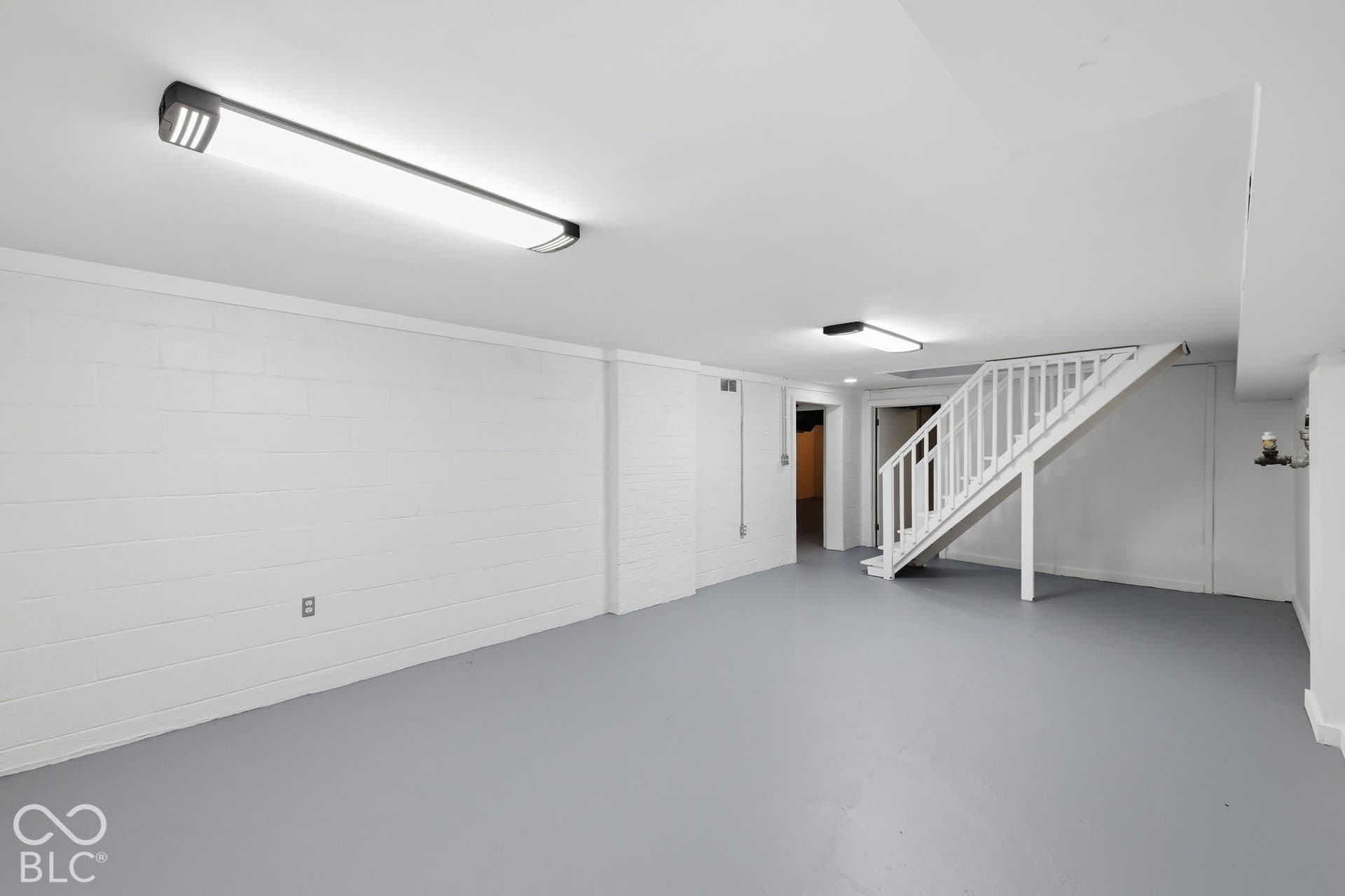 Expansive lower level featuring painted concrete block walls, painted concrete flooring, and a white wood-finish staircase with railings