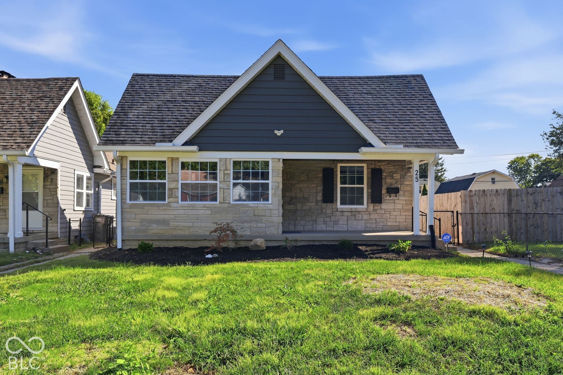 Gable roof with dark shingles, horizontal siding, stone veneer facade, covered front porch, and mature landscaping