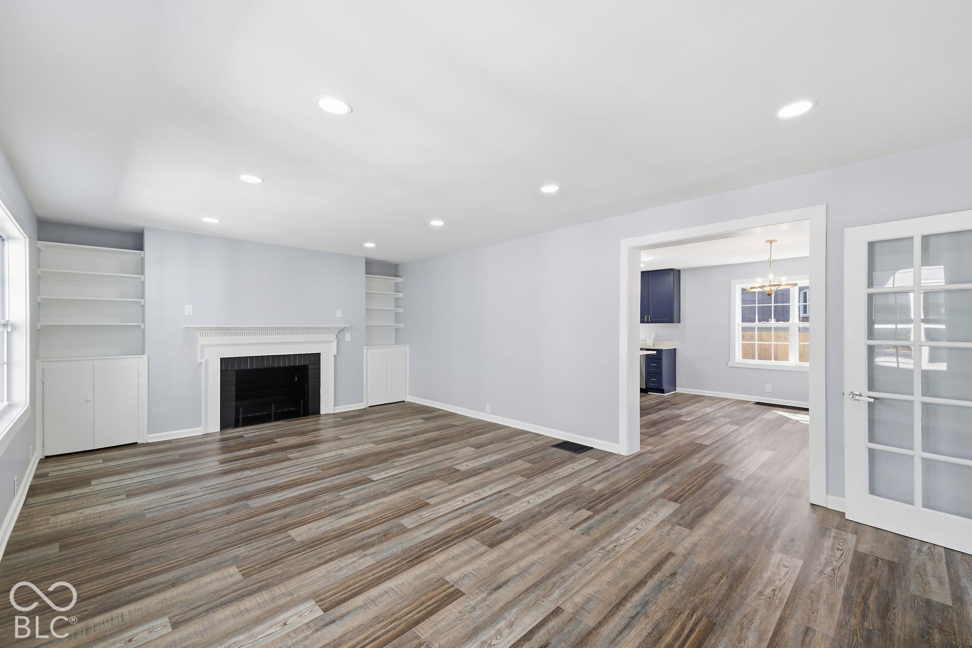 Recessed lighting illuminates the wood-finish flooring, built-in shelving, and a central fireplace with a white mantel