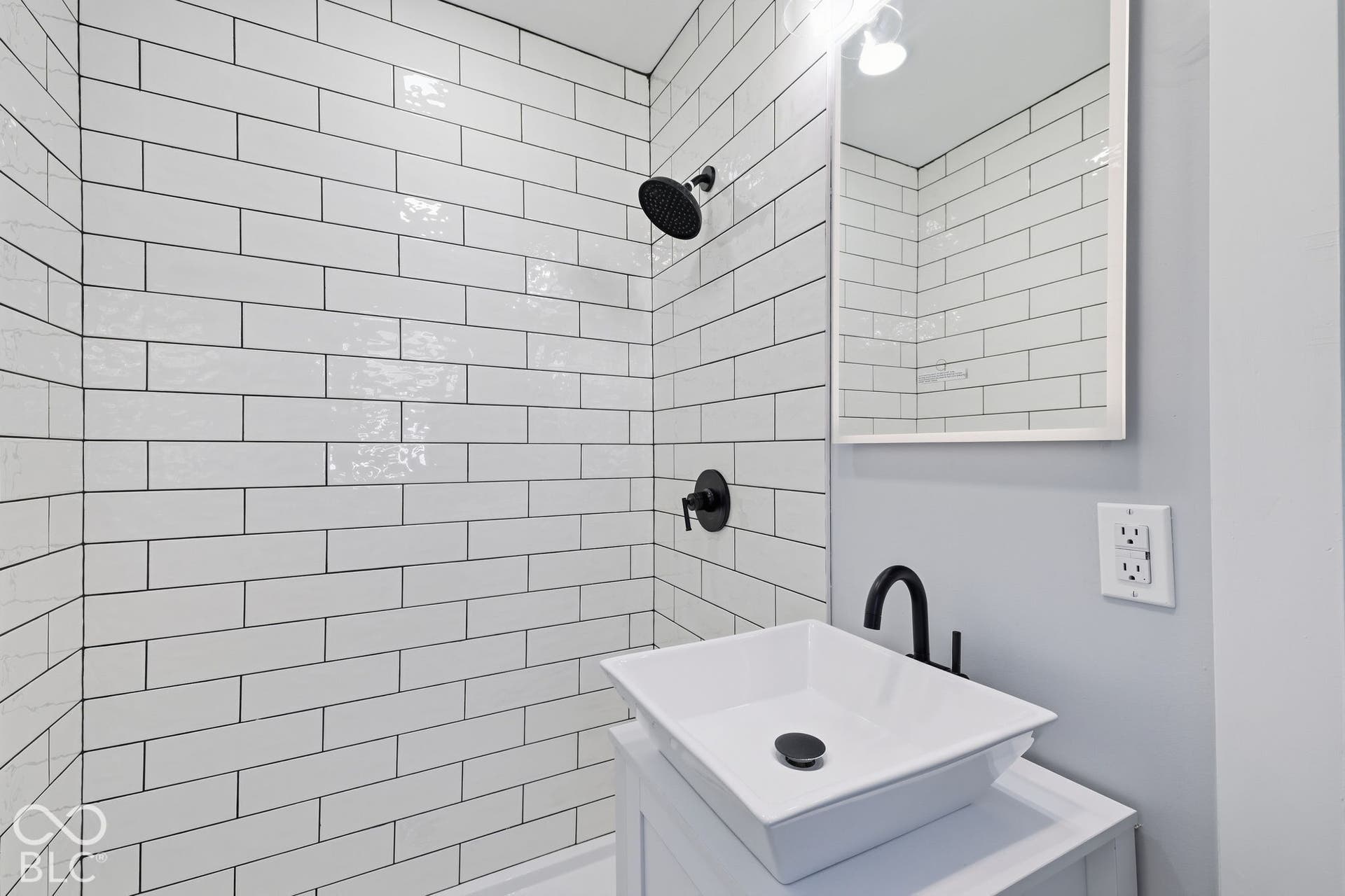 Subway tile shower surround with matte black fixtures, white rectangular vessel sink, coordinating matte black faucet, and vanity with integrated storage