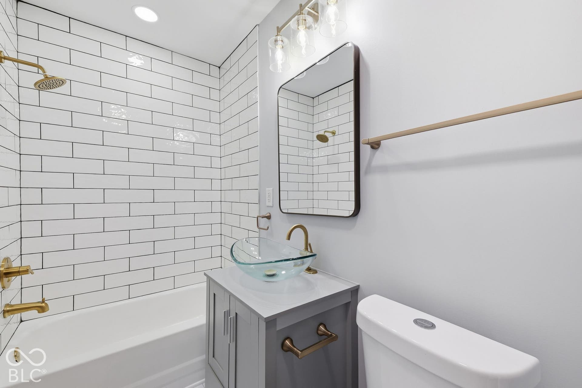 Bathroom featuring a white subway tile shower surround, brass-finish fixtures, a gray vanity with a vessel sink, and a rectangular mirror