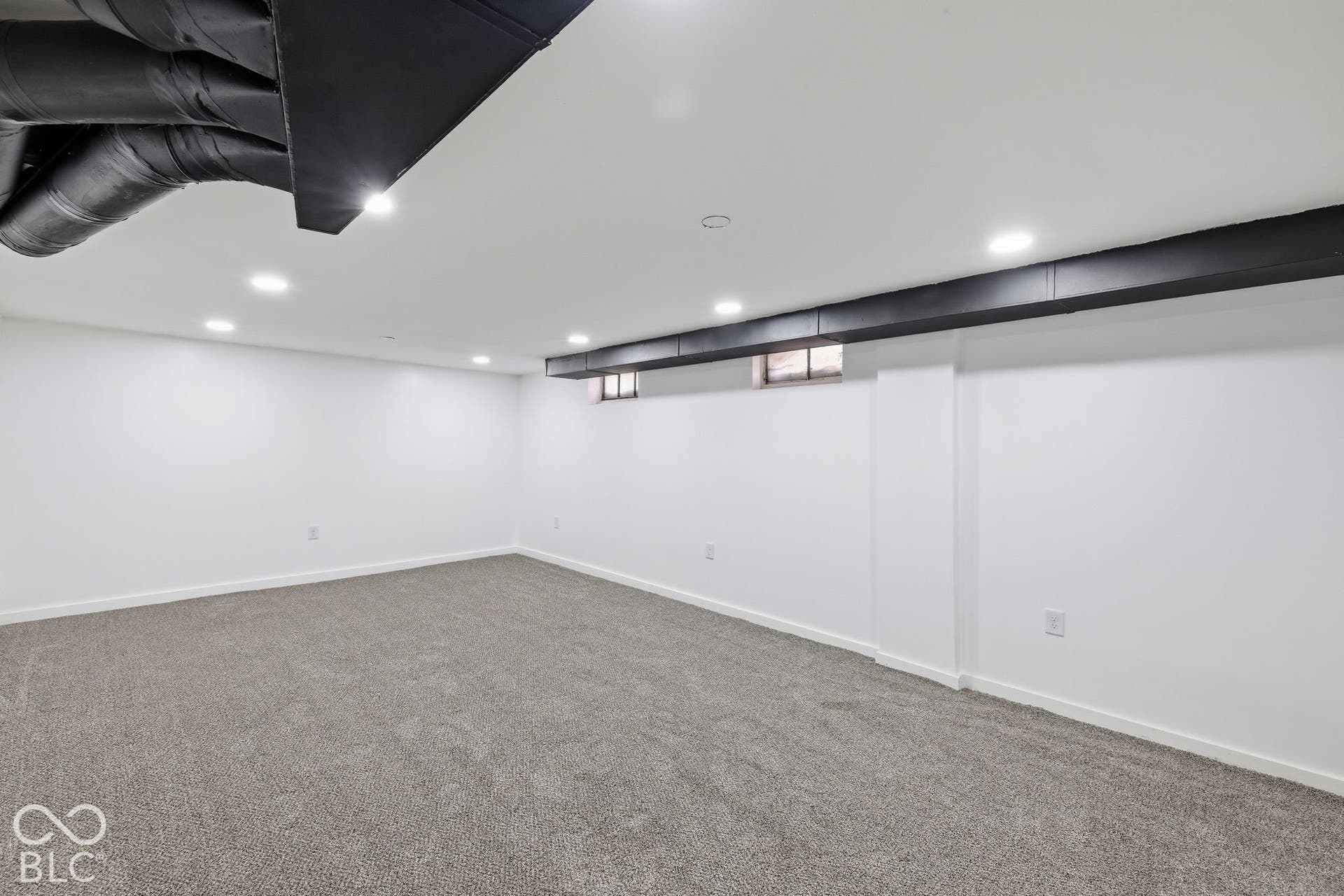 Recessed lighting illuminates the space, featuring white walls, gray carpeting, and exposed black ductwork
