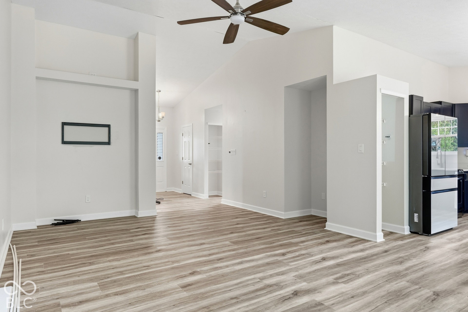 Vaulted ceiling with a ceiling fan, wood-finish flooring, white walls,