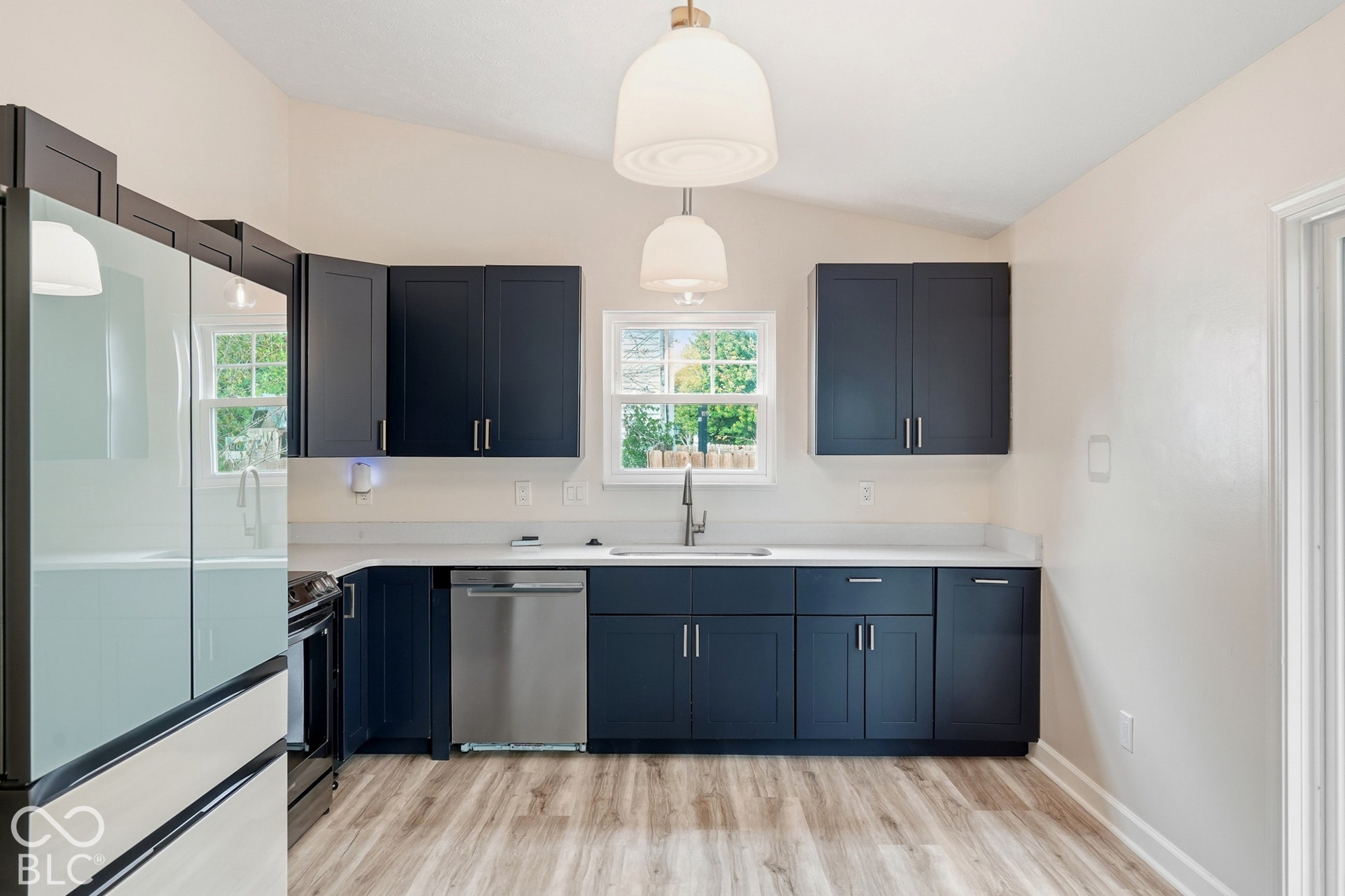 Kitchen featuring dark cabinetry, light countertops, wood-finish flooring, stainless steel appliances, and dual pendant lighting