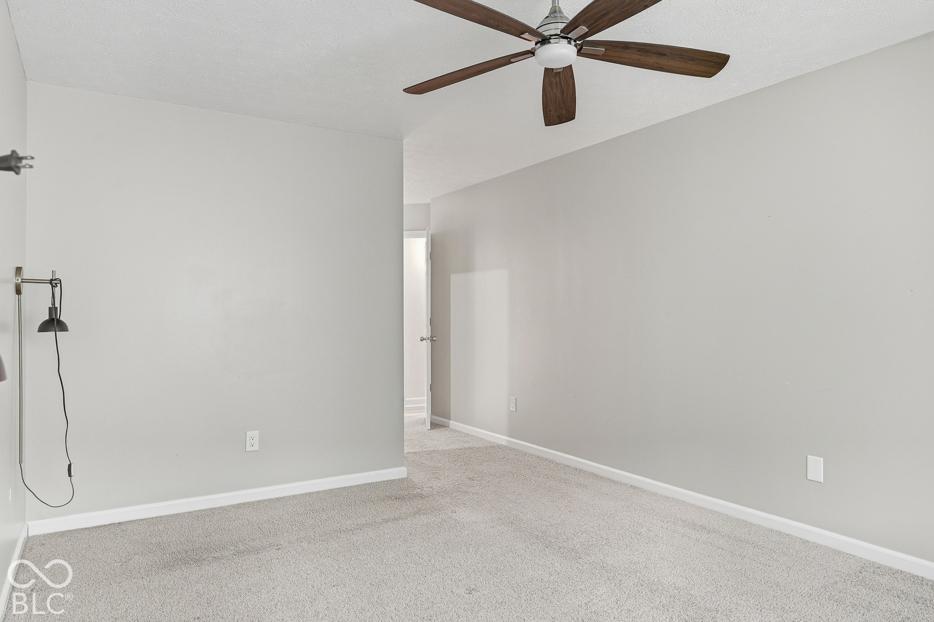 Light gray wall paint, textured ceiling, ceiling fan with wood-finish blades, light-colored carpet flooring, and white trim