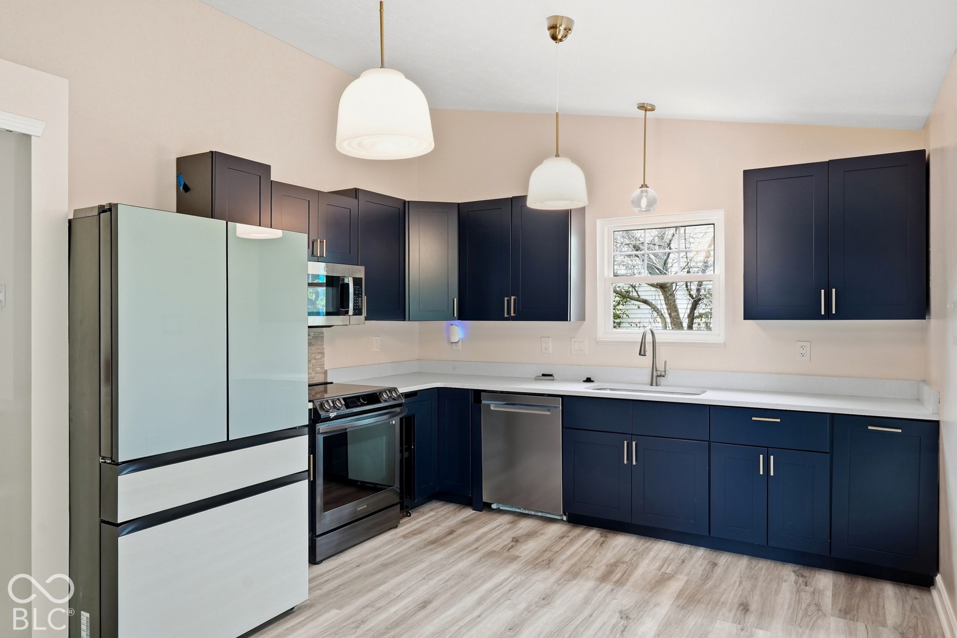 Kitchen featuring dark blue cabinetry, white countertops, wood-finish flooring, stainless steel appliances, and pendant lighting