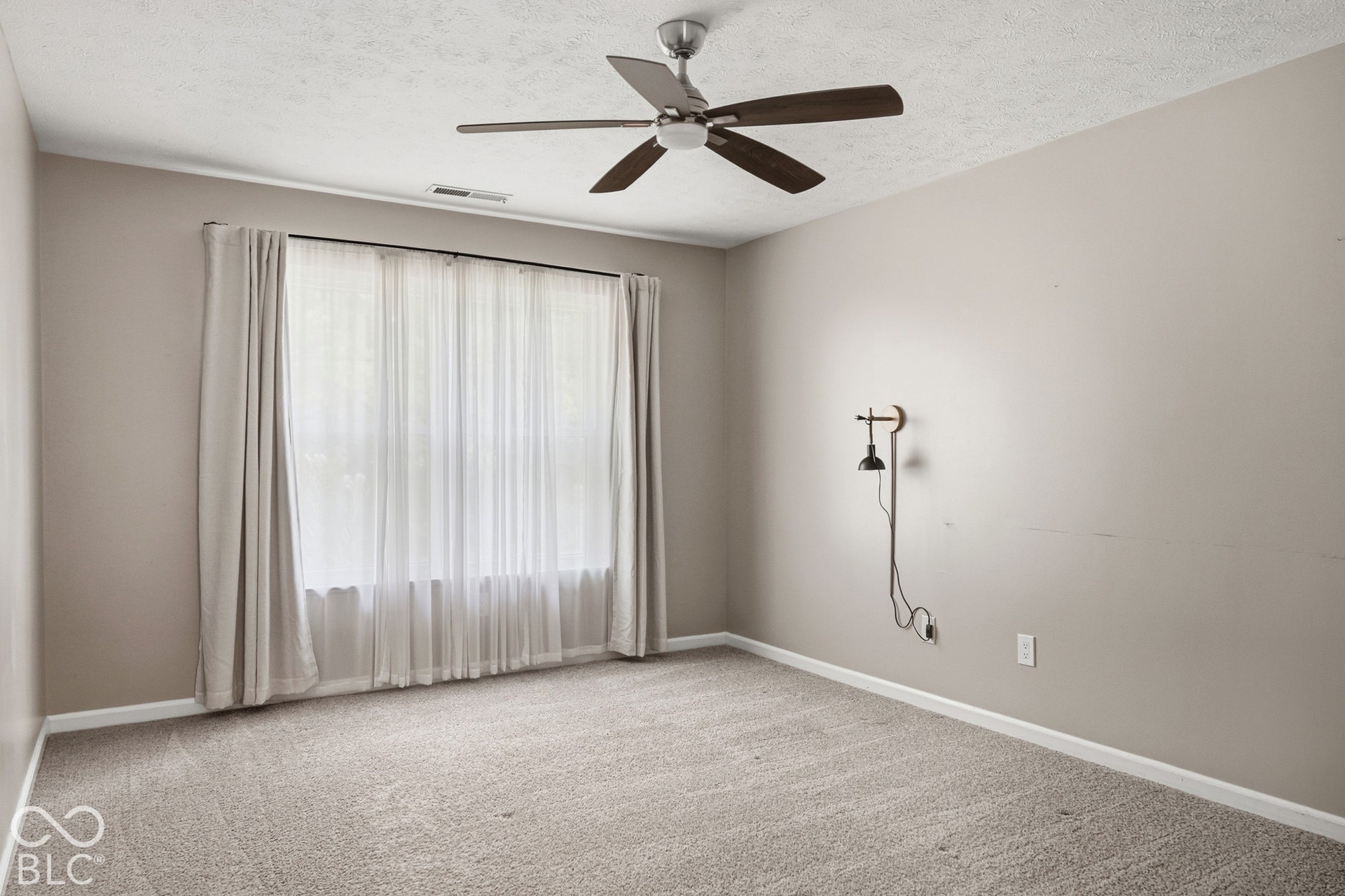 Textured carpeting, neutral wall color, ceiling fan with wood-finish blades, and a large picture window