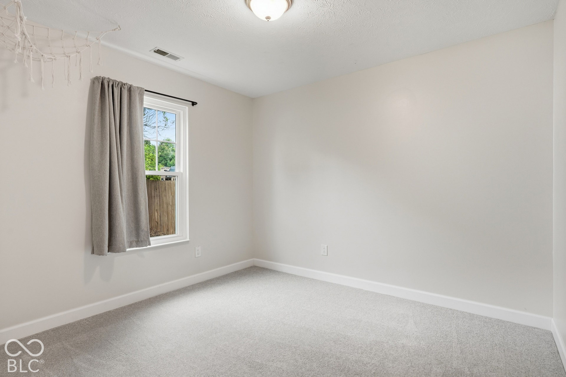 Light gray carpeting, a single window with white trim, and a white ceiling light fixture