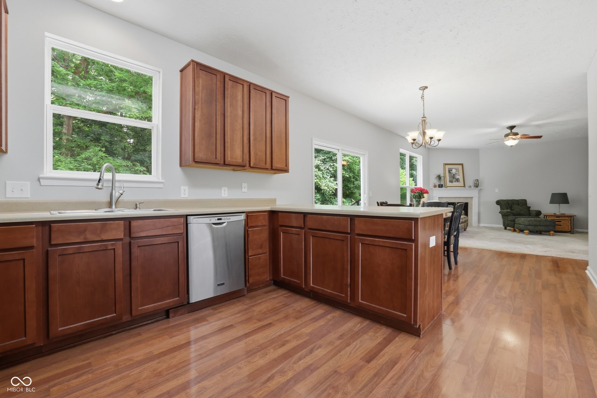 Open concept entertaining from your Kitchen to living room. Kitchen featuring wood-finish flooring, a stainless steel dishwasher, and rich wood cabinetry