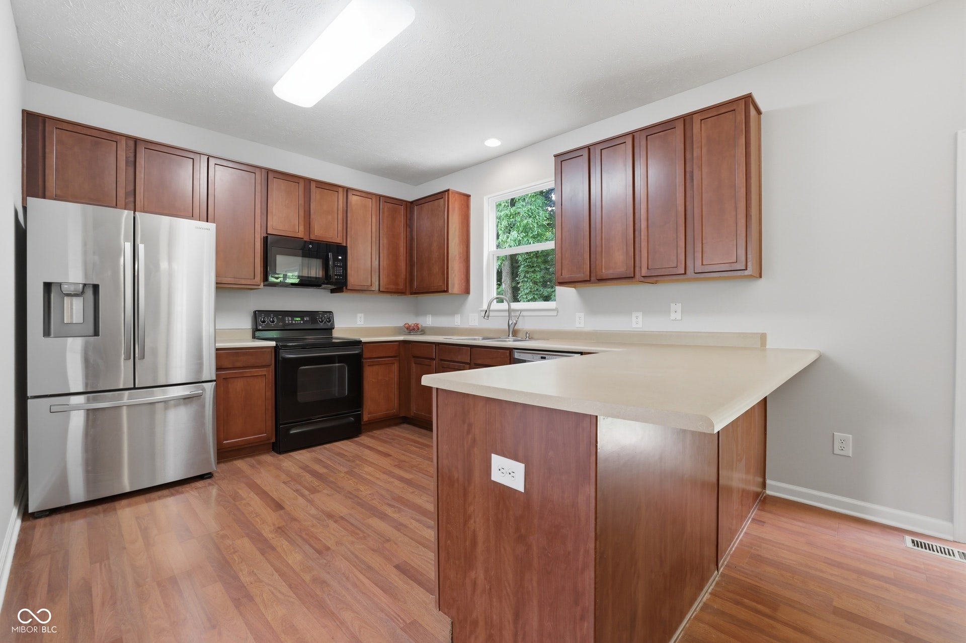 Spacious kitchen featuring wood-finish flooring, abundant cabinetry, stone-look countertops, stainless steel refrigerator, and integrated dishwasher