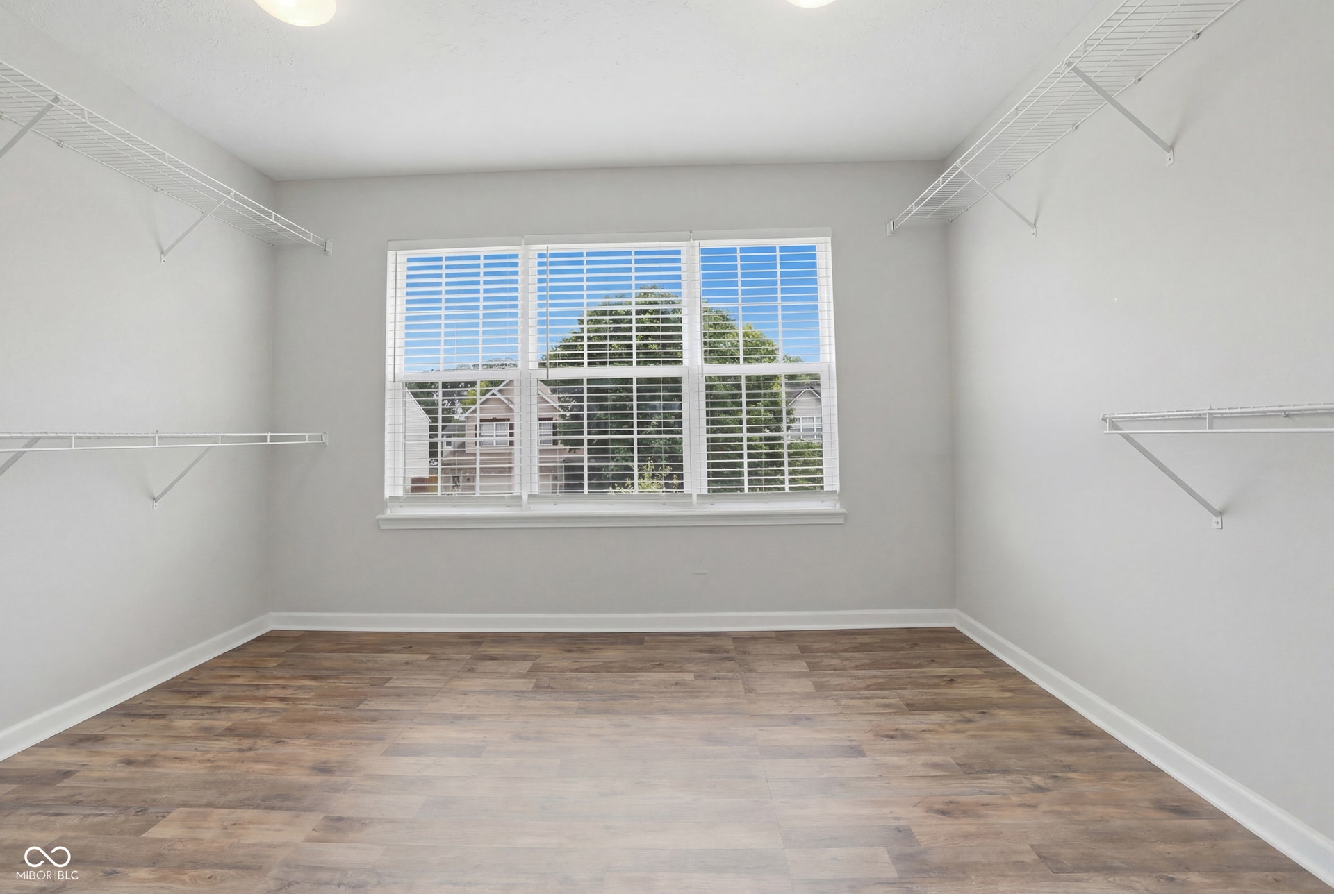 Spacious room featuring wood-finish flooring, white baseboards, and a large window with horizontal blinds