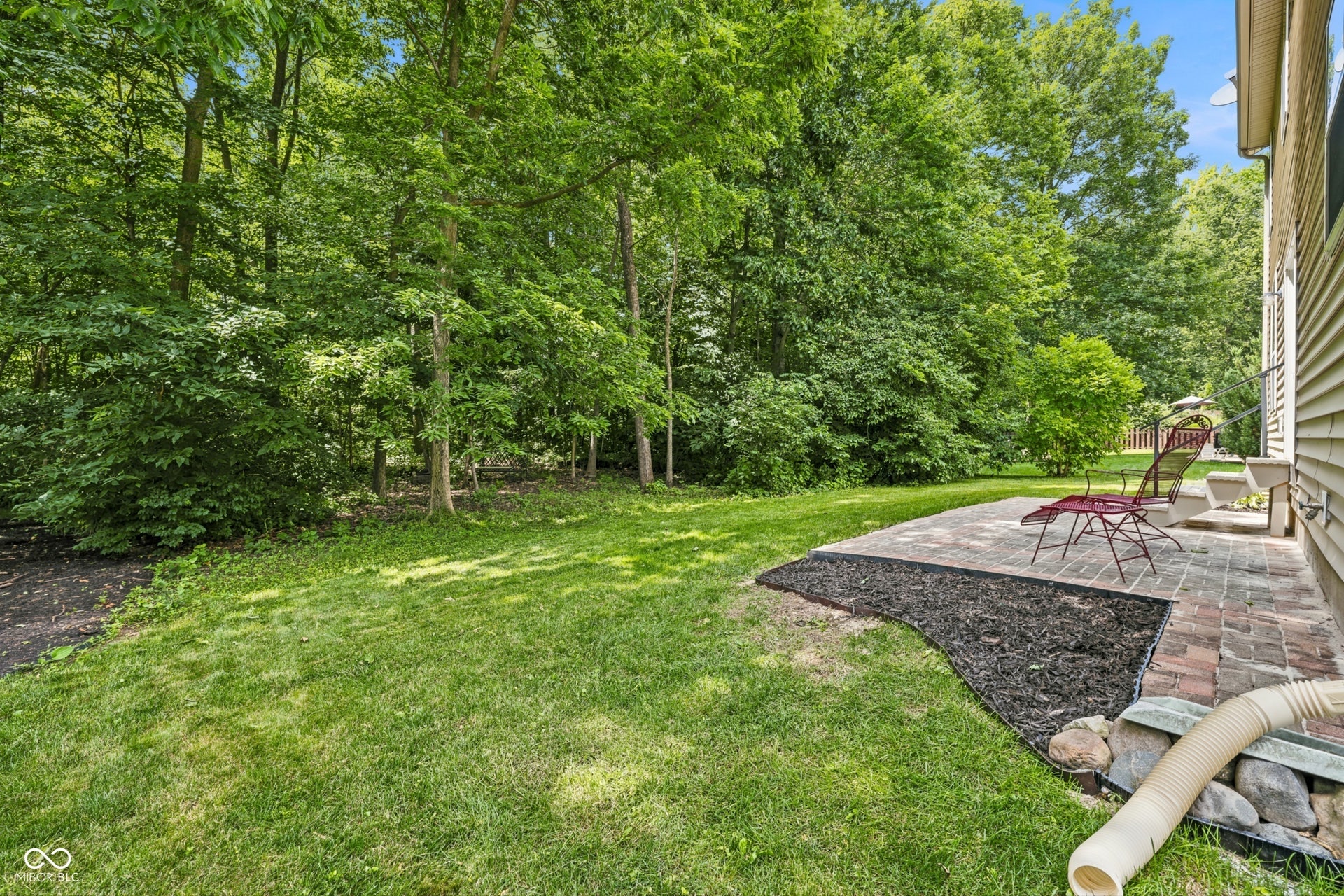 Private grassy yard with mature trees, a paver patio, brick edging, and a mulched garden beds