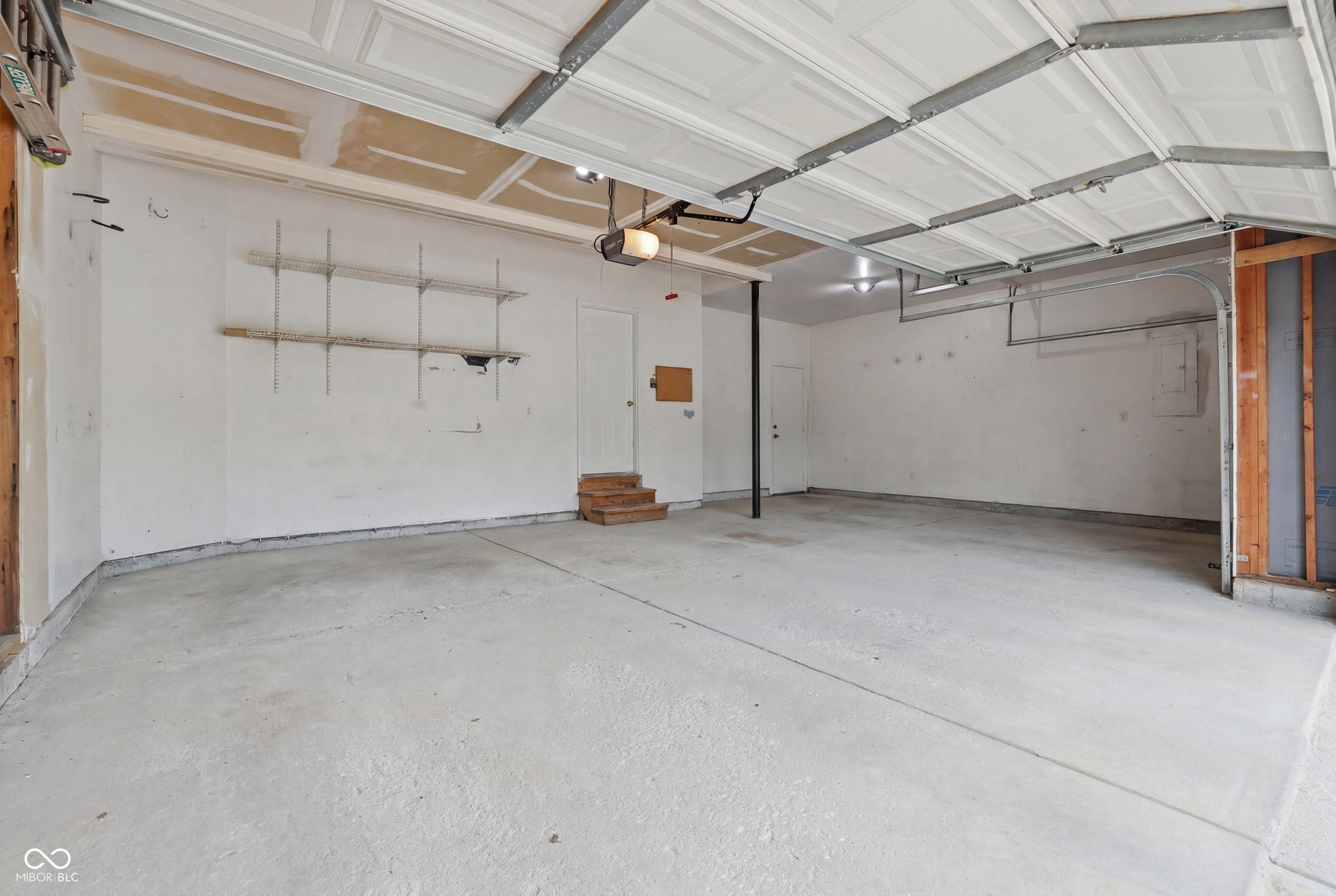 Spacious three-car garage with overhead door mechanism, concrete flooring, and interior access door and service door to backyard