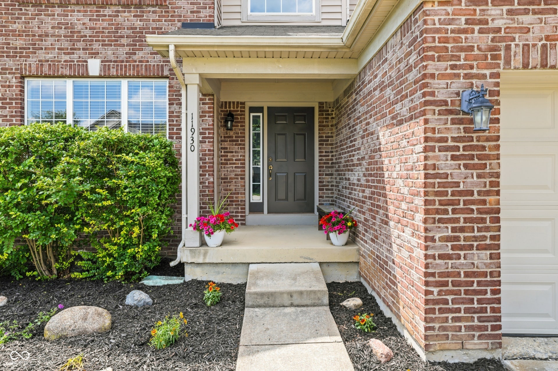 Brick facade exterior featuring a covered entry, concrete walkway, white-trimmed windows with horizontal blinds, and an attached garage