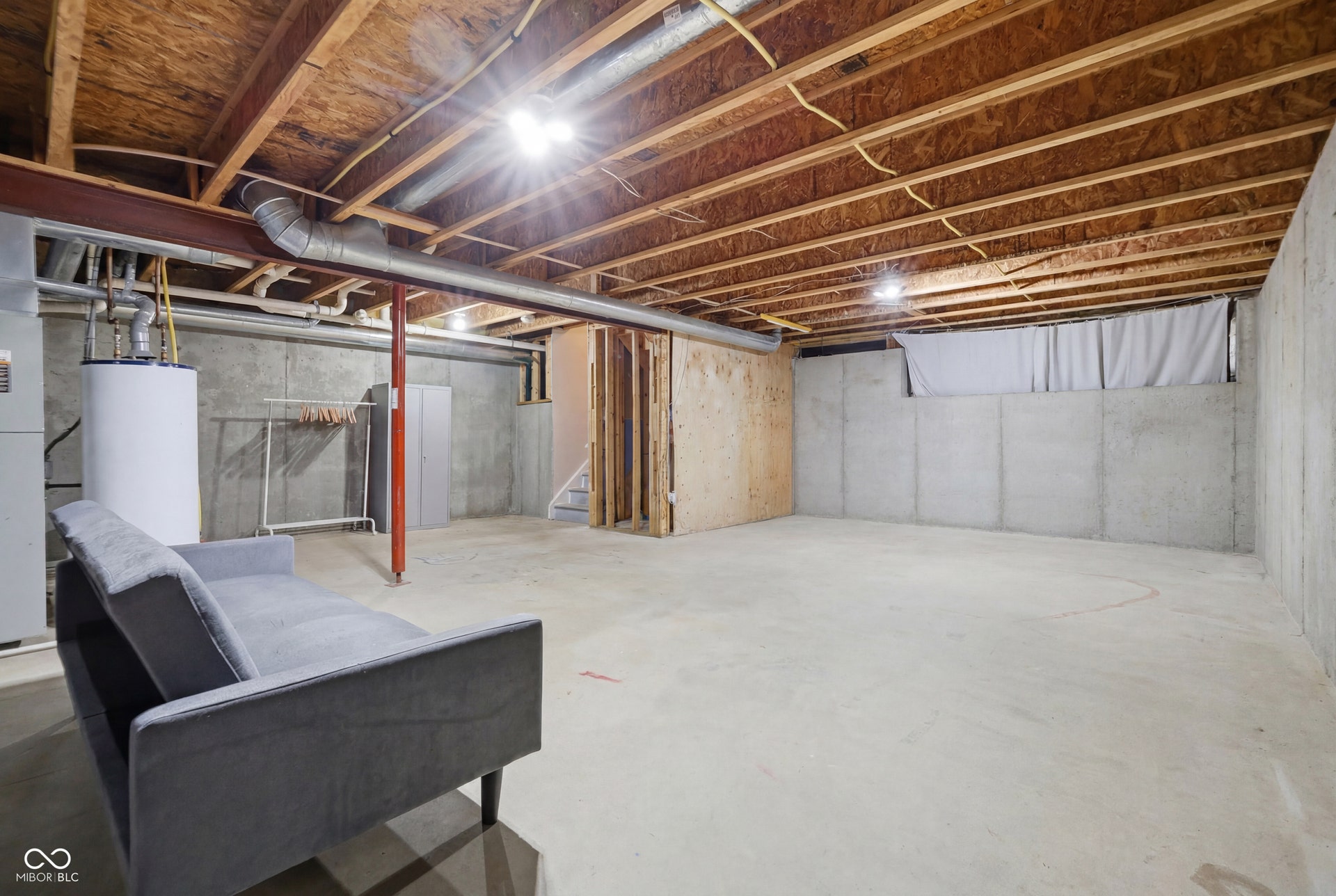 Unfinished basement featuring concrete walls and flooring, exposed wood ceiling joists, and overhead lighting
